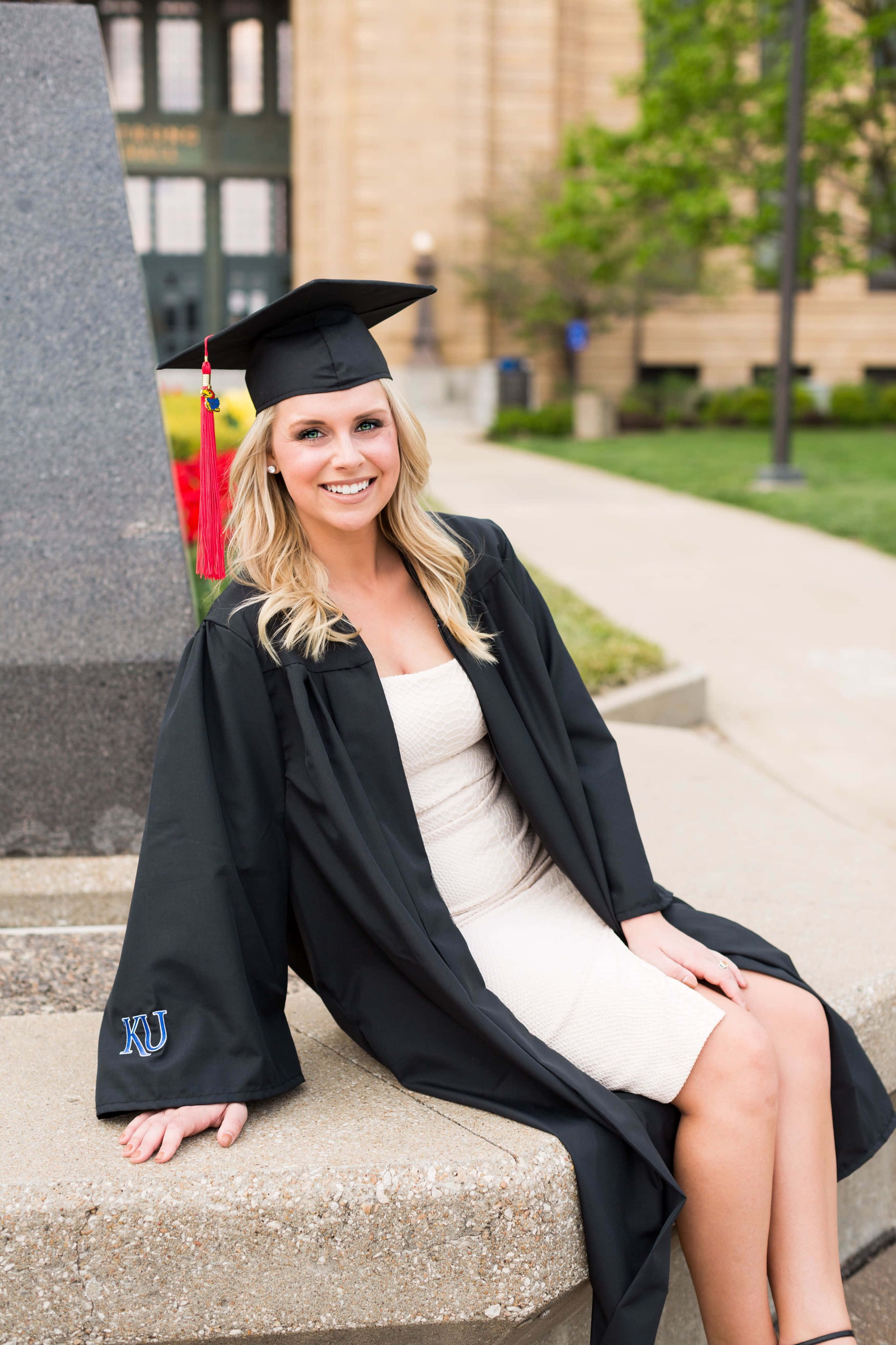 Graduation 桌布 壁紙 — 一位微笑的金髮女性，身穿黑色畢業帽和長袍，帶紅色流蘇，坐在戶外的石階上。