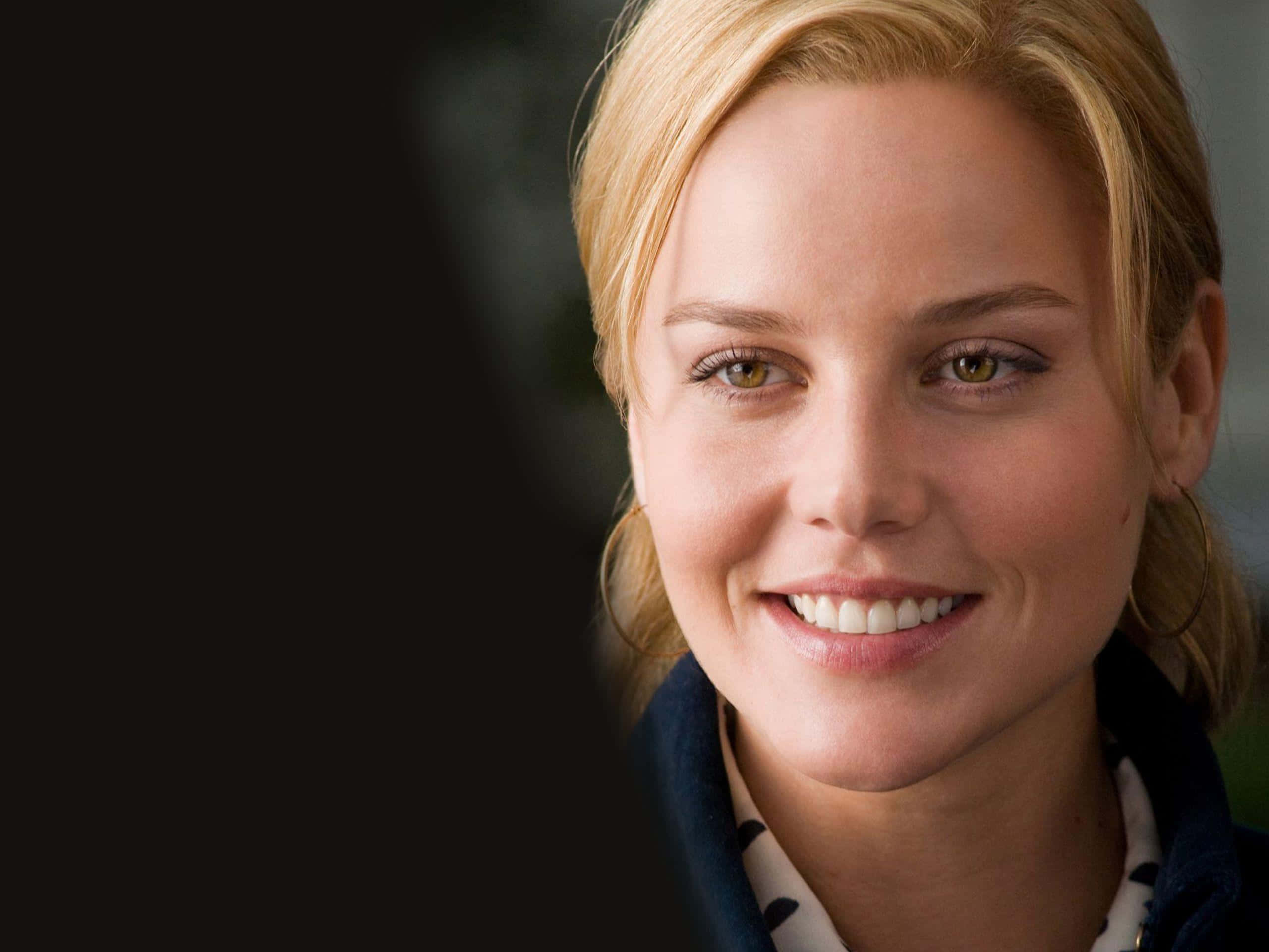 Abbie Cornish 桌布 壁紙 — 一位微笑的金髮女性的特寫肖像，擁有溫暖的棕色眼睛和柔和的燈光，背景為深色。