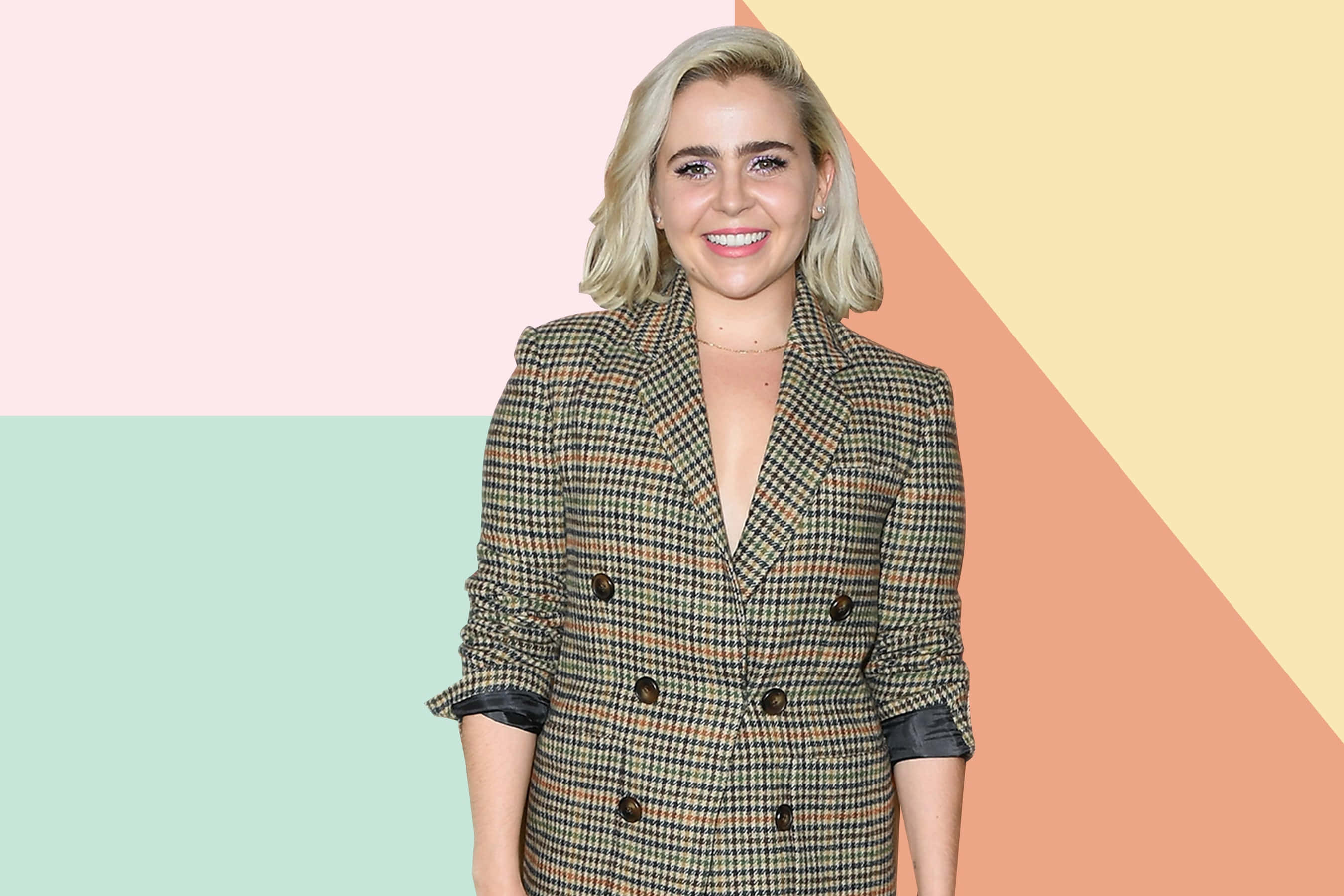 Mae Whitman 桌布 壁紙 — 一位微笑的金髮女性穿著千鳥格西裝外套，站在粉彩幾何背景前。