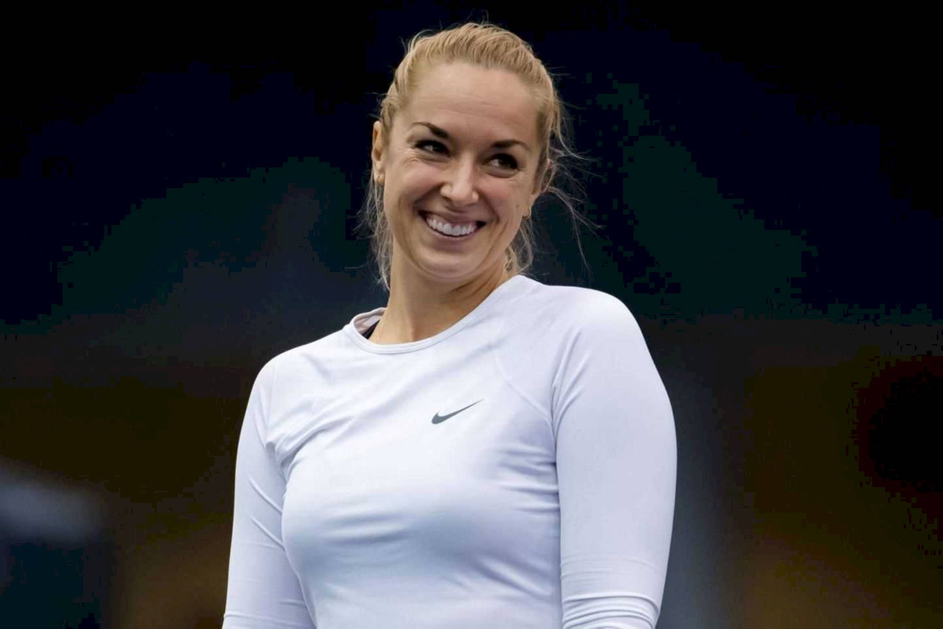 Smile 桌布 壁紙 — 一位微笑的金髮女性穿著白色長袖Nike運動衫，站在模糊的深色背景前。