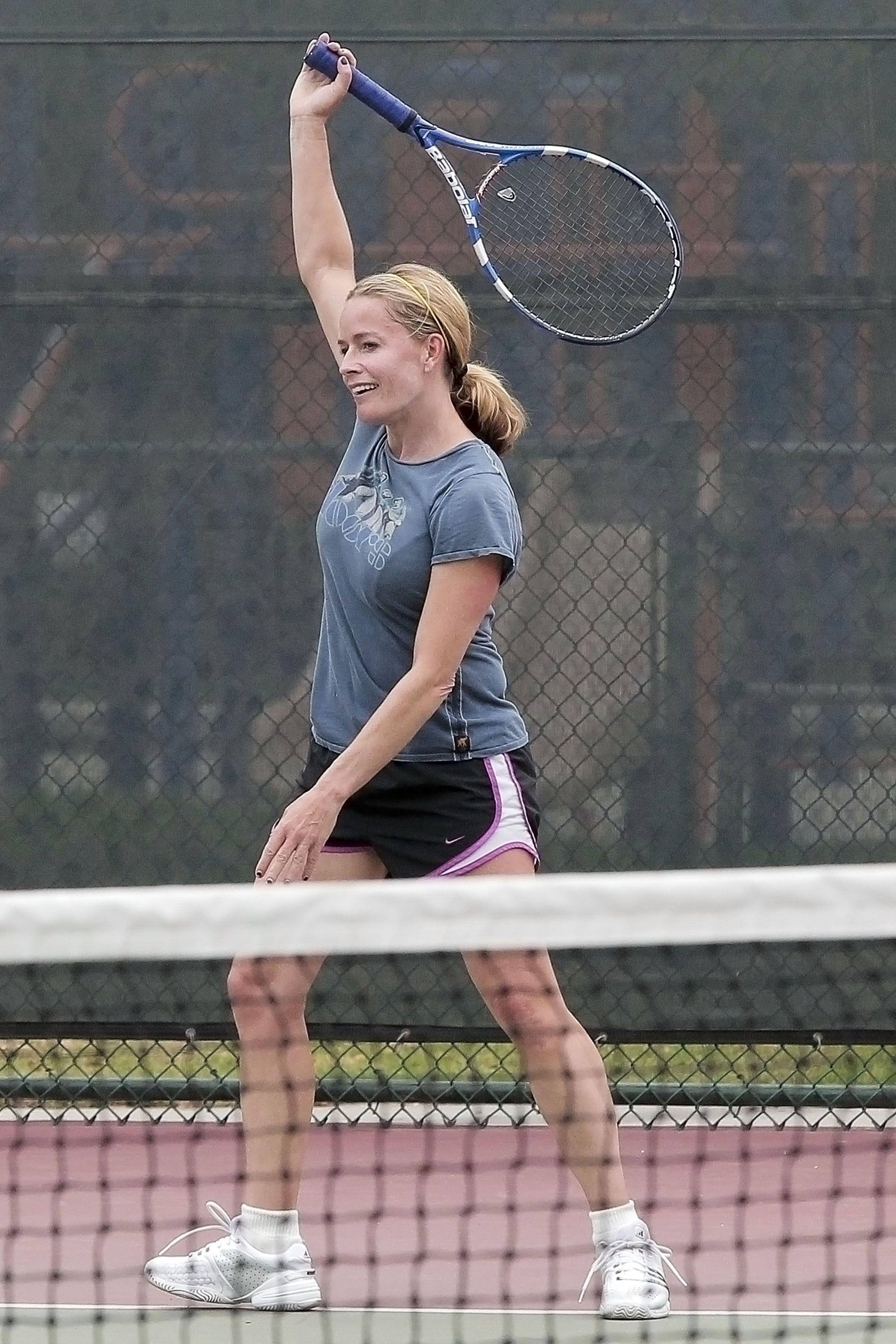 Tennis 桌布 壁紙 — 一位微笑的金髮女性穿著運動服，在球場上勝利地將藍色網球拍舉過頭頂。