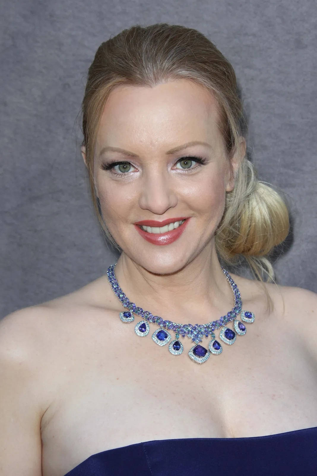 Celebrity 桌布 壁紙 — 一位微笑的金髮女性身穿海軍藍無肩帶連衣裙，在灰色背景下佩戴一條耀眼的藍色和銀色寶石項鍊。