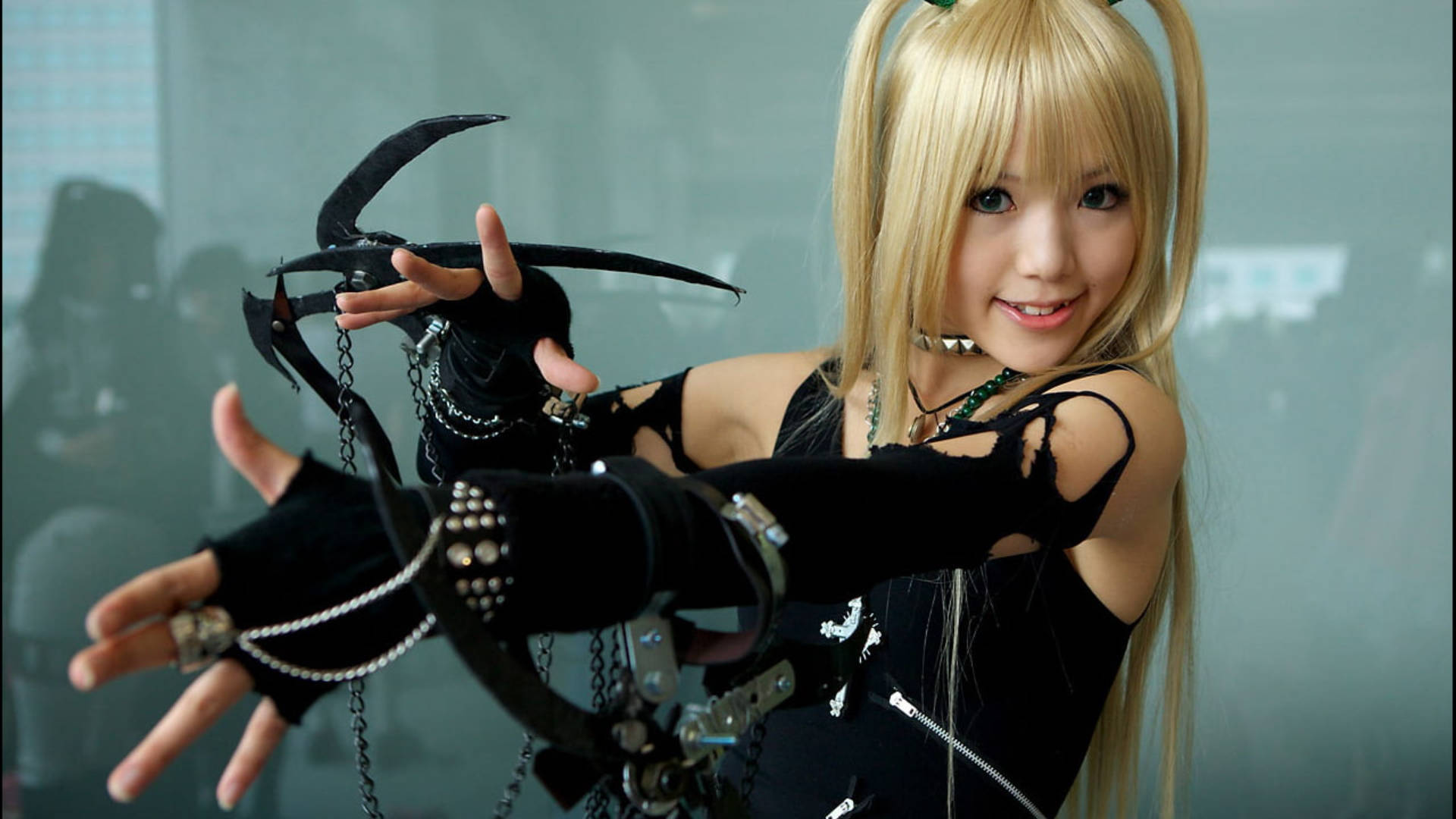 Misa 桌布 壁紙 — 一位微笑的金髮女性身穿黑色哥德式cosplay，自信地揮舞著一把華麗的大型爪狀武器。