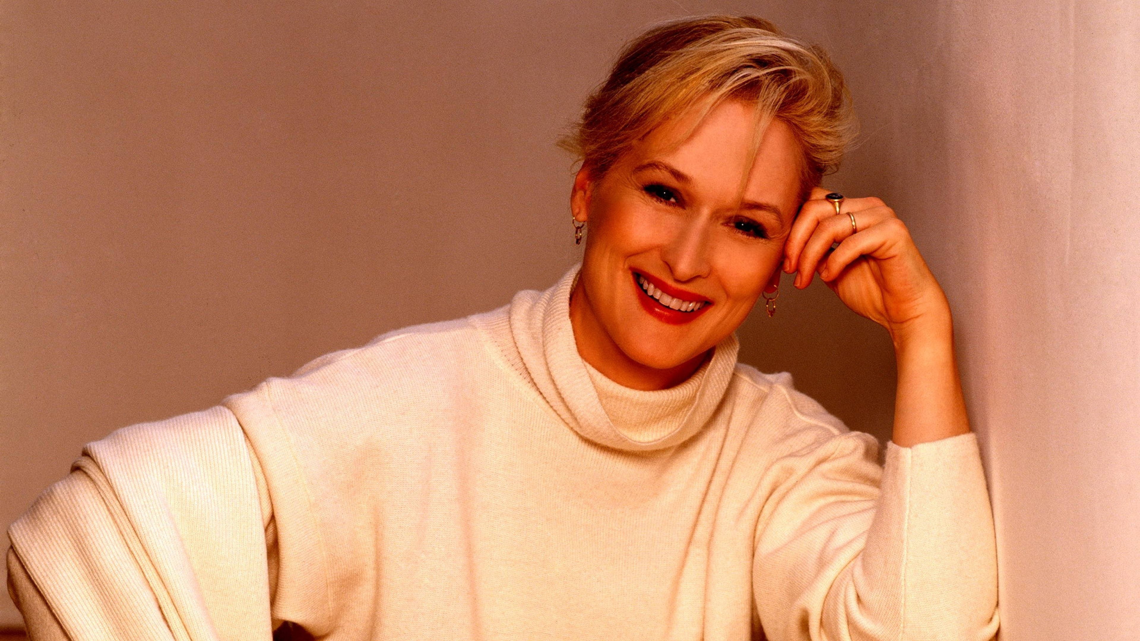 Meryl Streep 桌布 壁紙 — 一位微笑的金髮女性靠著牆，身穿奶油色高領毛衣。