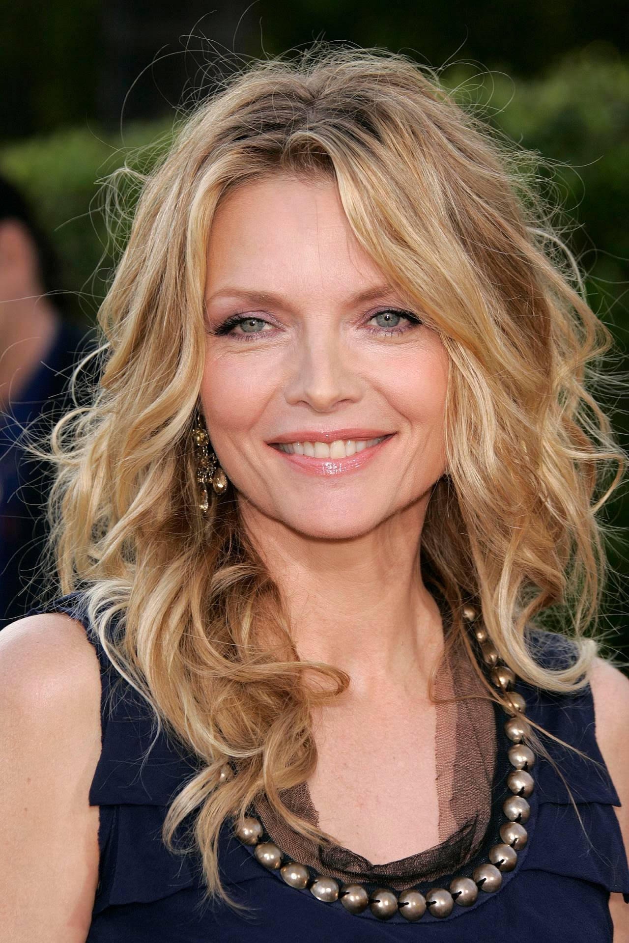 Celebrity 桌布 壁紙 — 一位微笑的金髮波浪長髮女性身穿深藍色連衣裙和珠鏈項鍊的特寫肖像。