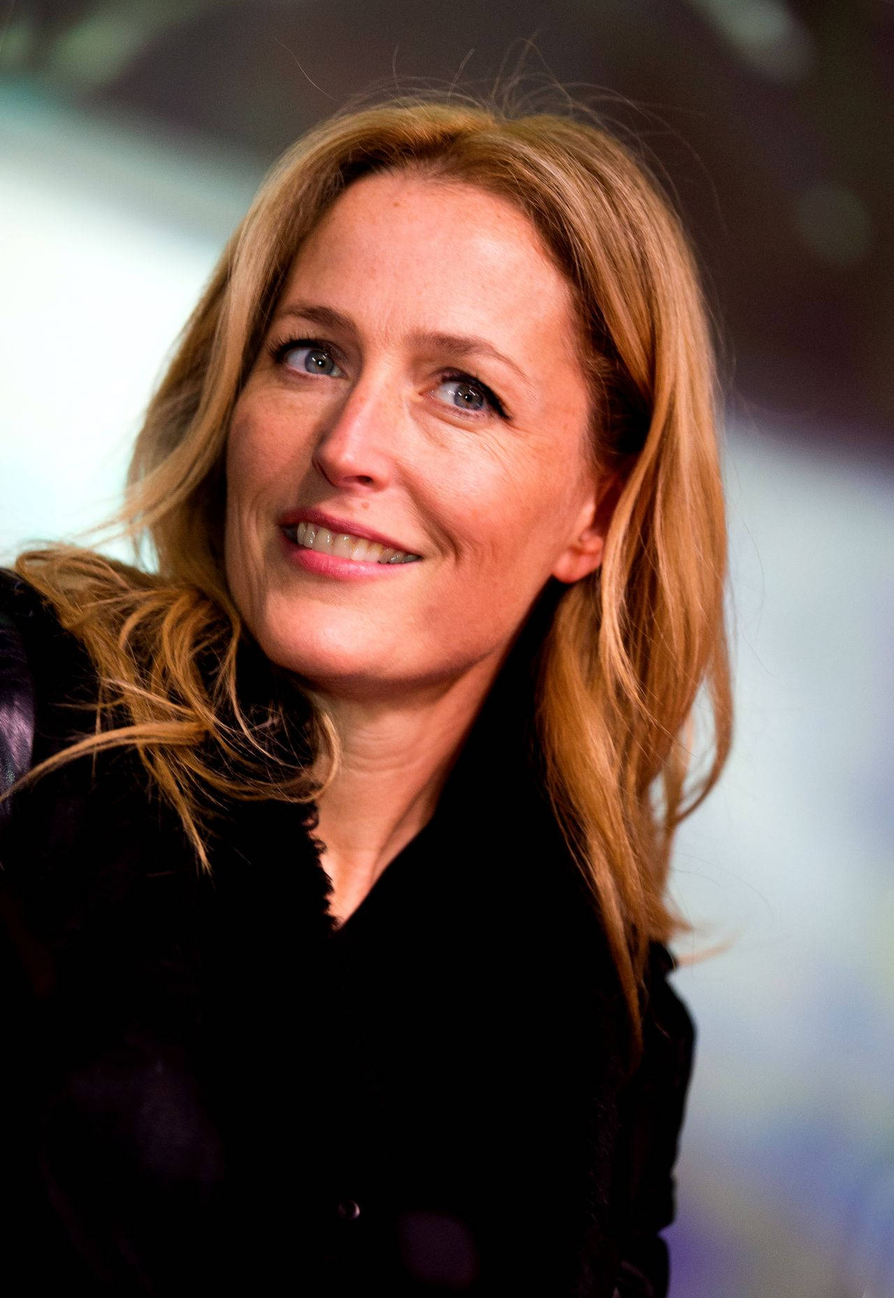 gillian anderson 桌布 壁紙 — 一位微笑的金髮碧眼女性穿著黑色上衣的特寫肖像。