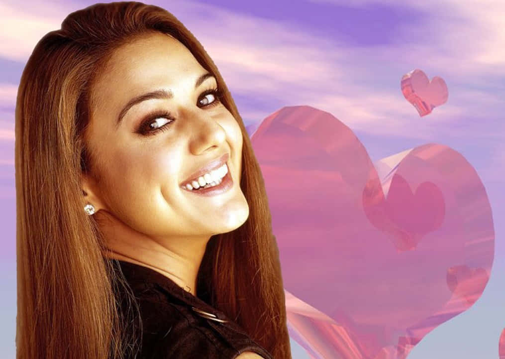 Preity Zinta 桌布 壁紙 — 一位微笑的長棕髮女性，背景是夢幻的紫色天空，漂浮著粉紅色水晶心形。