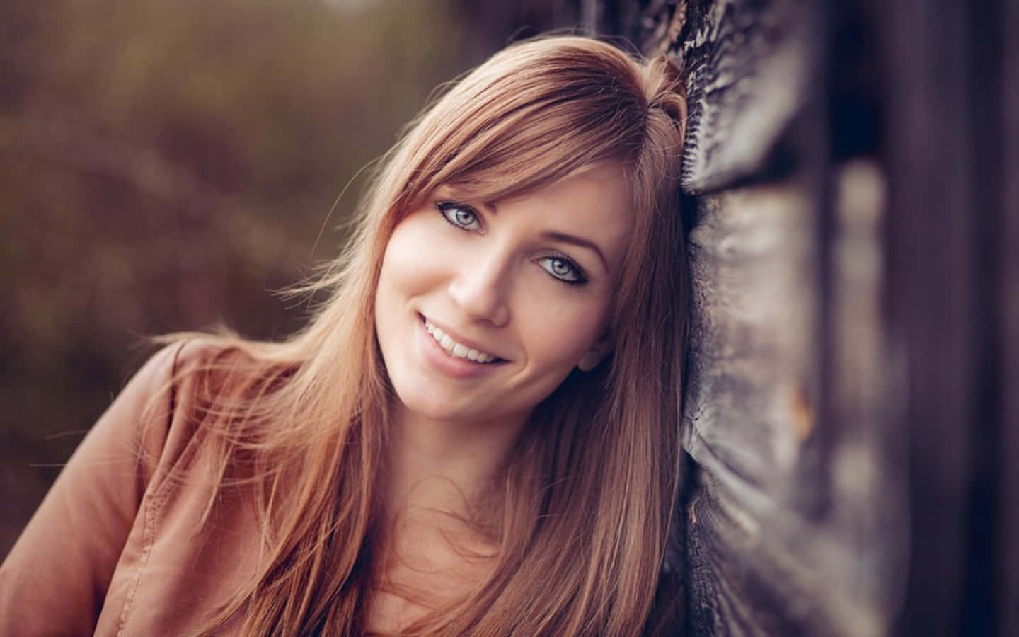 Smile 桌布 壁紙 — 一位微笑的長金髮女性在柔和自然光中靠著風化的木柵欄。
