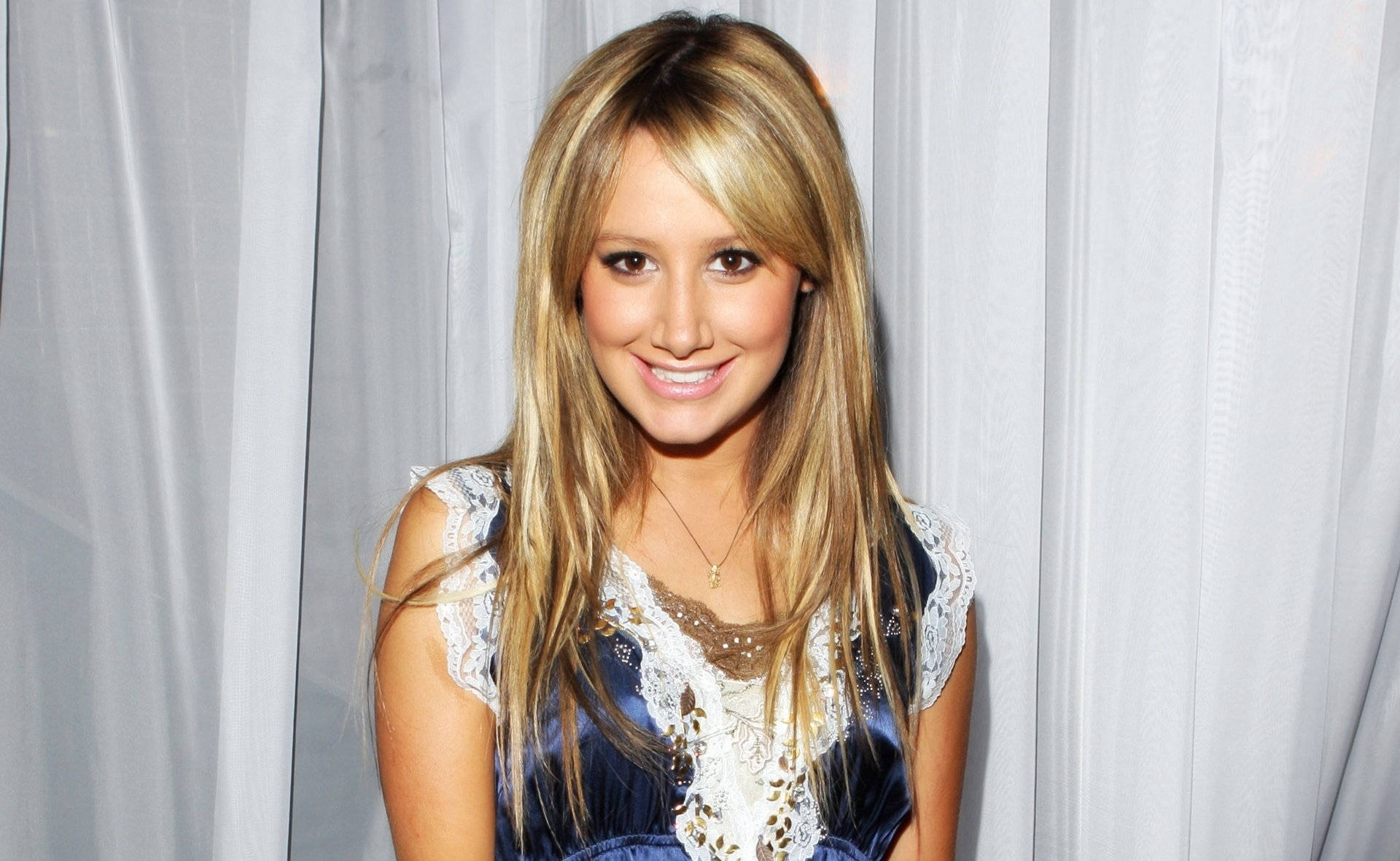 Ashley Tisdale 桌布 壁紙 — 一位微笑的長金髮女性穿著藍色蕾絲上衣，背景是白色窗簾。