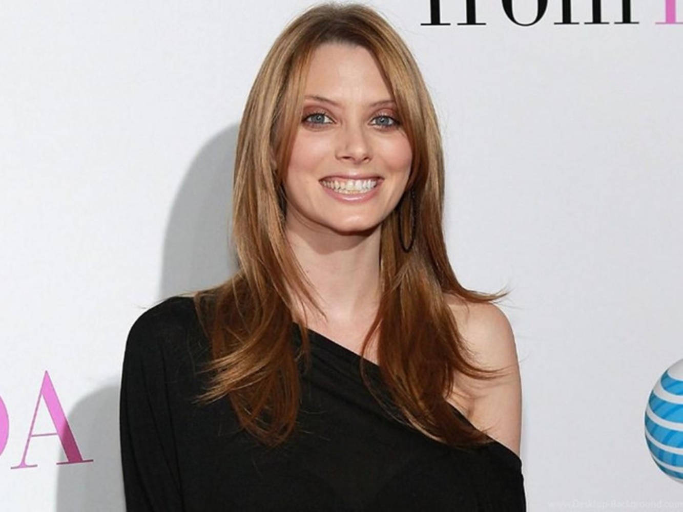 Celebrity 桌布 壁紙 — 一位微笑的長髮棕髮女性，在帶有標誌的白色背景前穿著黑色單肩上衣。