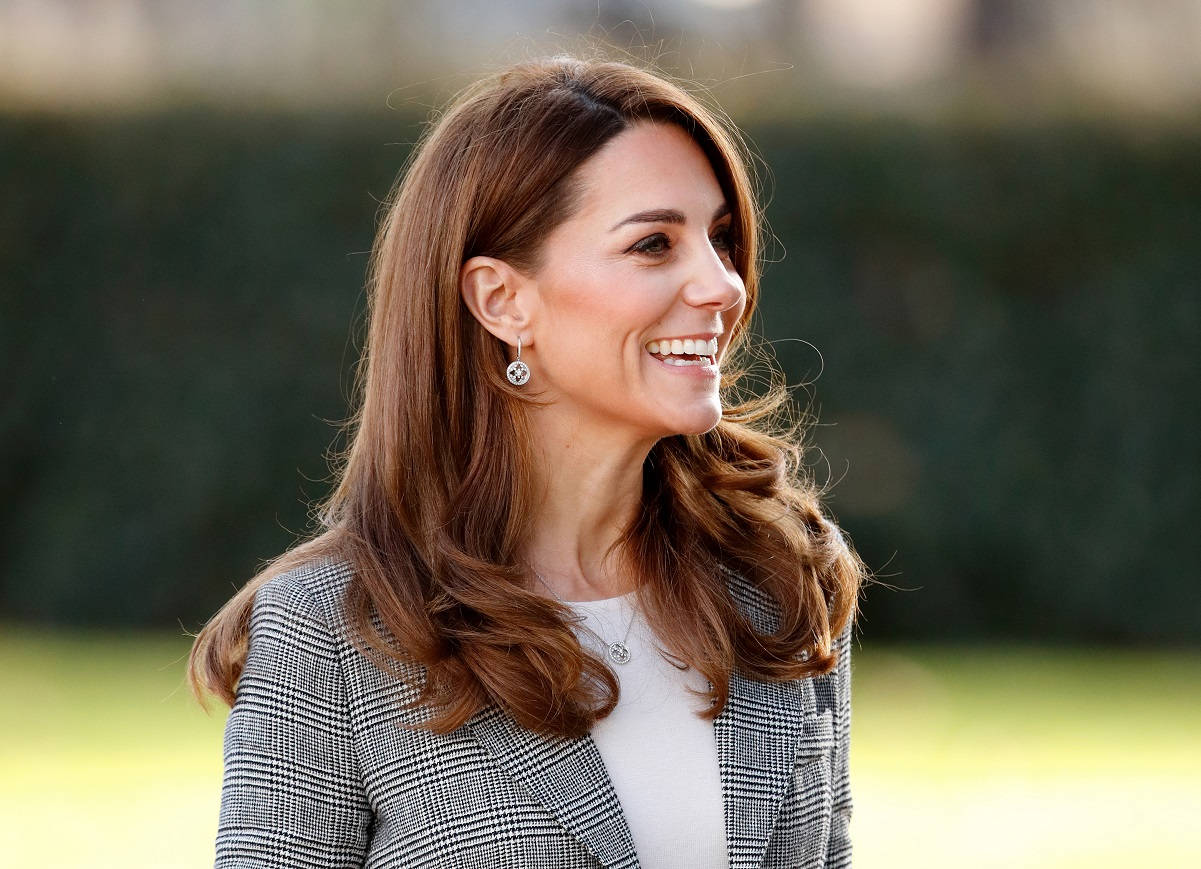 Kate Middleton 桌布 壁紙 — 一位微笑的長髮棕髮女性，在戶外穿著格子西裝外套，背景是模糊的綠色樹籬。