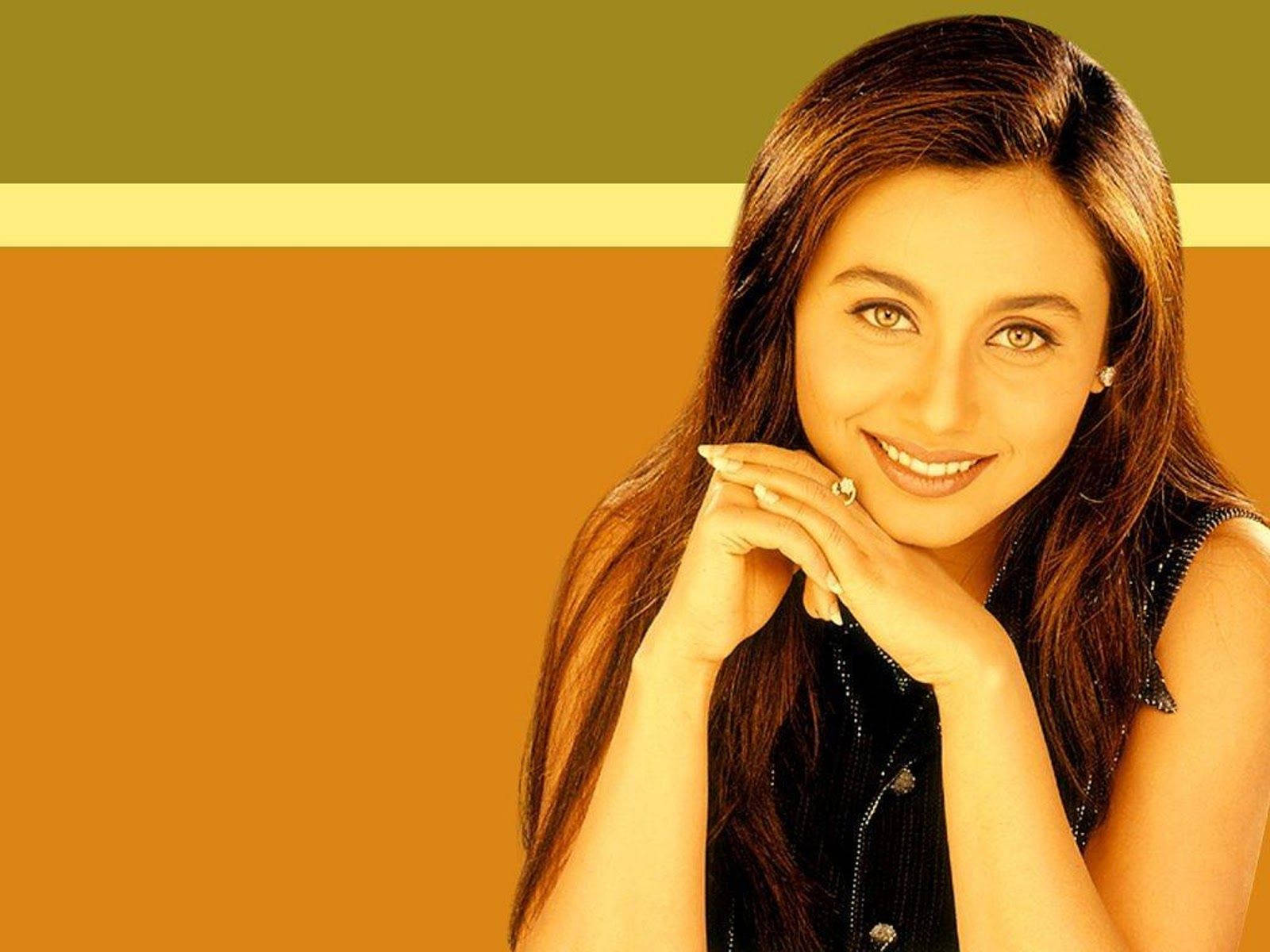 Rani Mukerji 桌布 壁紙 — 一位微笑的長髮棕髮女性，雙手托腮，背景是溫暖的橙色和橄欖綠條紋。