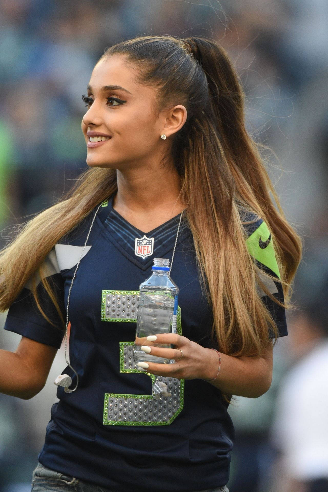 Seattle Seahawks 桌布 壁紙 — 一位微笑的長髮馬尾辮女性，身穿西雅圖海鷹隊球衣，在體育場內拿著水瓶。