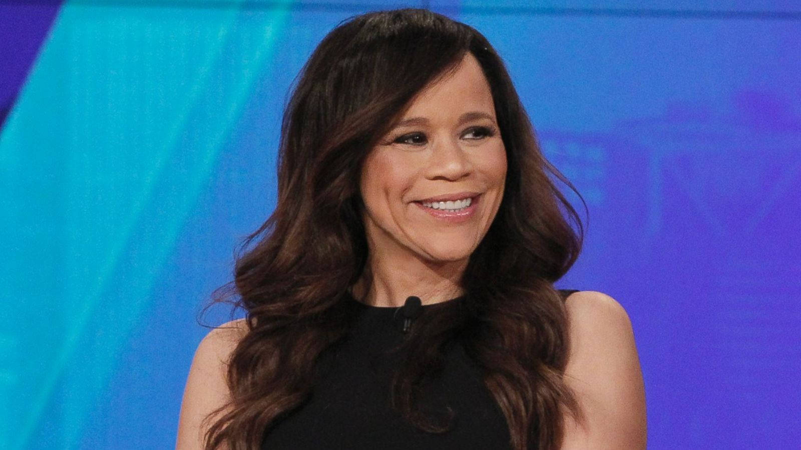 Celebrity 桌布 壁紙 — 一位微笑的長黑髮女性，穿著黑色上衣，背景是充滿活力的藍色漸變色。