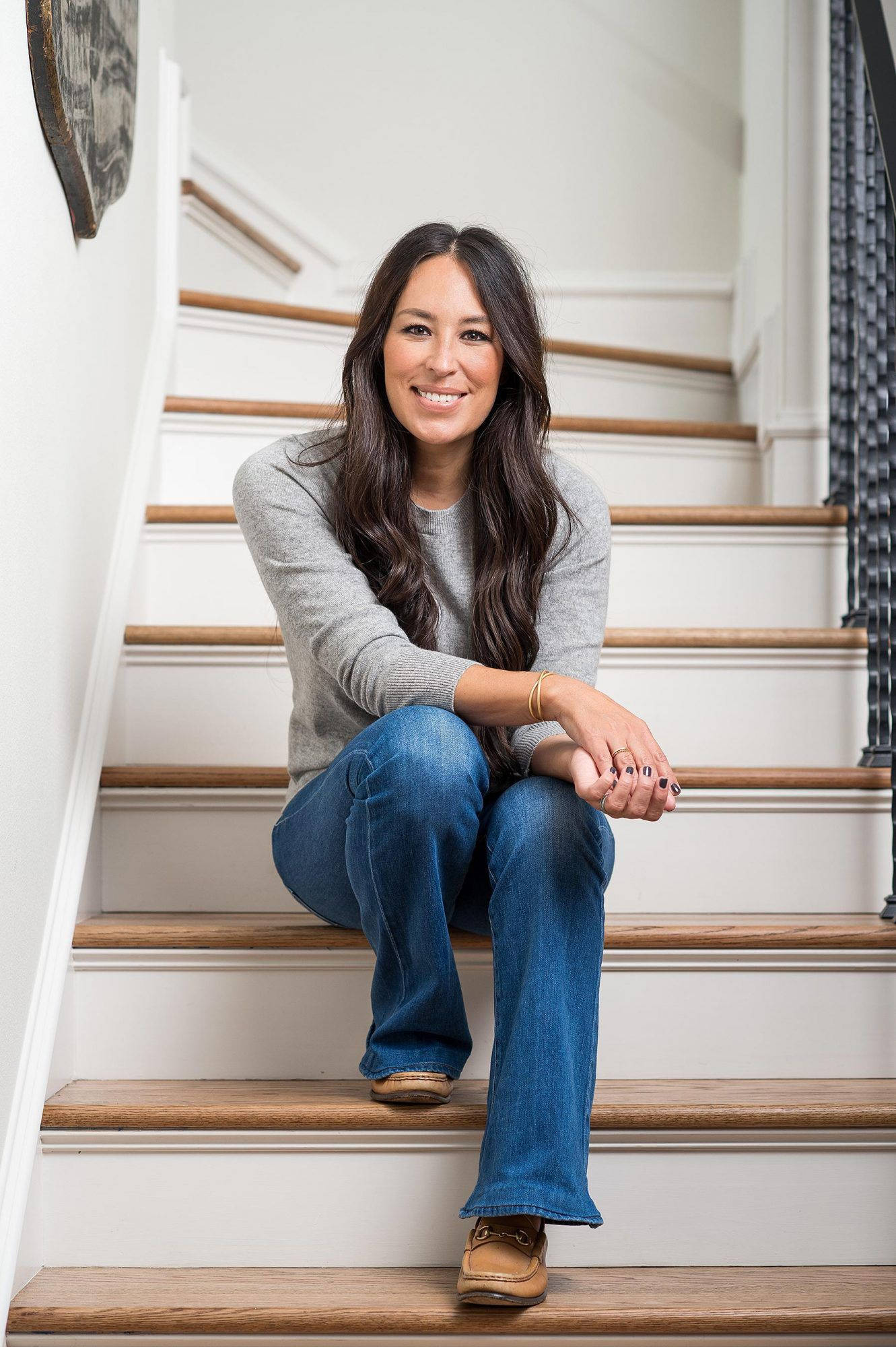 Joanna 桌布 壁紙 — 一位微笑的長黑髮女性隨意地坐在帶有木質踏板的白色樓梯上，穿著灰色毛衣和藍色牛仔褲。