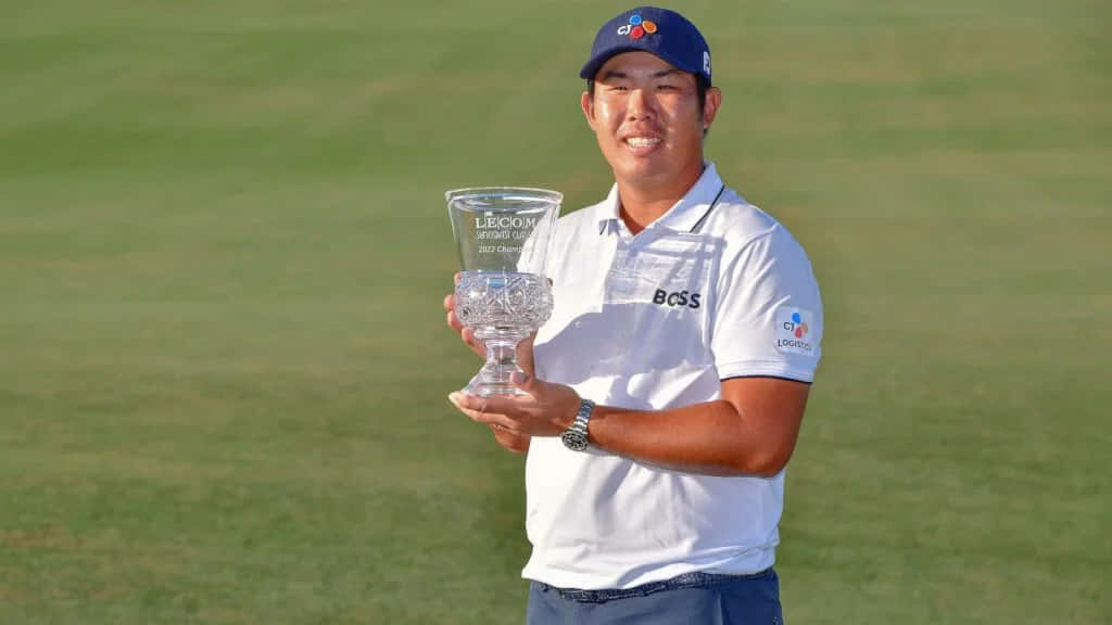 Trophy 桌布 壁紙 — 一位微笑的高爾夫球手在陽光明媚的綠色高爾夫球場上自豪地舉起水晶獎盃。