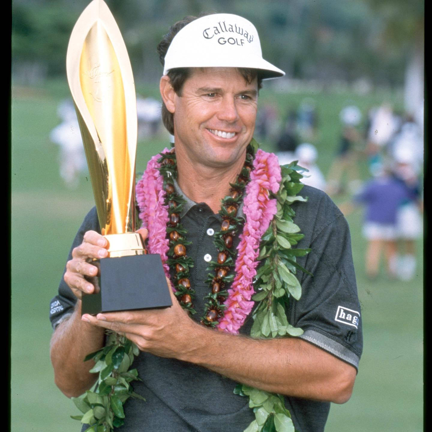 Trophy 桌布 壁紙 — 一位微笑的高爾夫球手在陽光明媚的高爾夫球場上，自豪地舉起金色獎盃，脖子上戴著粉綠相間的花環。