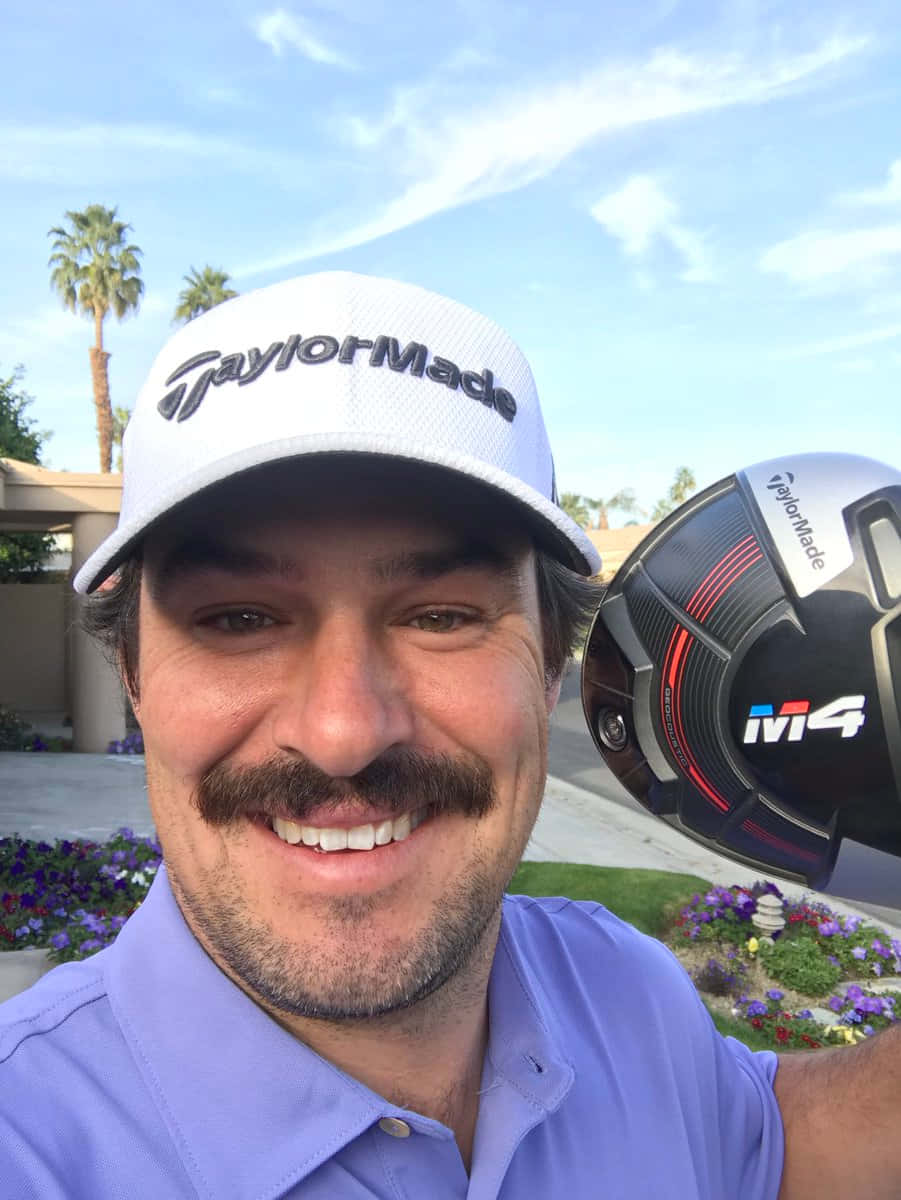 桌布 壁紙 — 一位微笑的高爾夫球手戴著白色TaylorMade帽子，在陽光明媚、有棕櫚樹和色彩繽紛花朵的背景前，手持一支黑色和紅色的M4開球木桿。