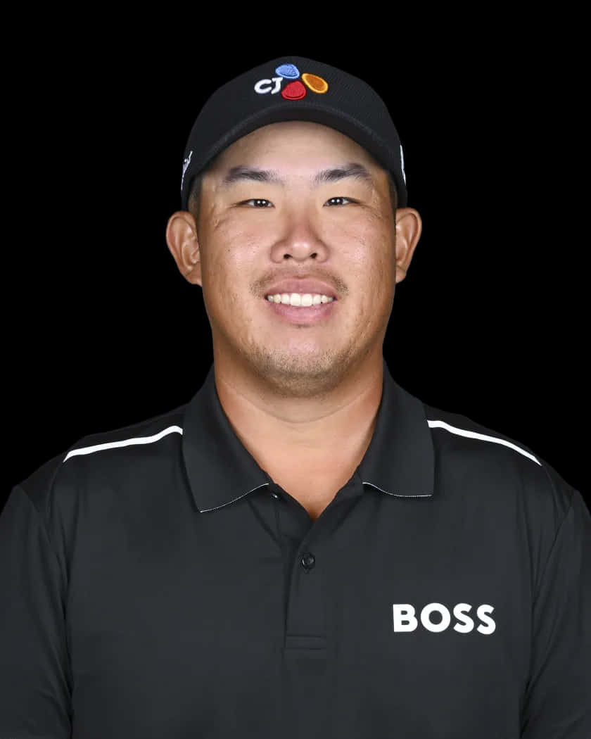 運動 桌布 壁紙 — 一位微笑的高爾夫球手戴著黑色帽子和BOSS Polo衫，在純黑色背景前擺姿勢。