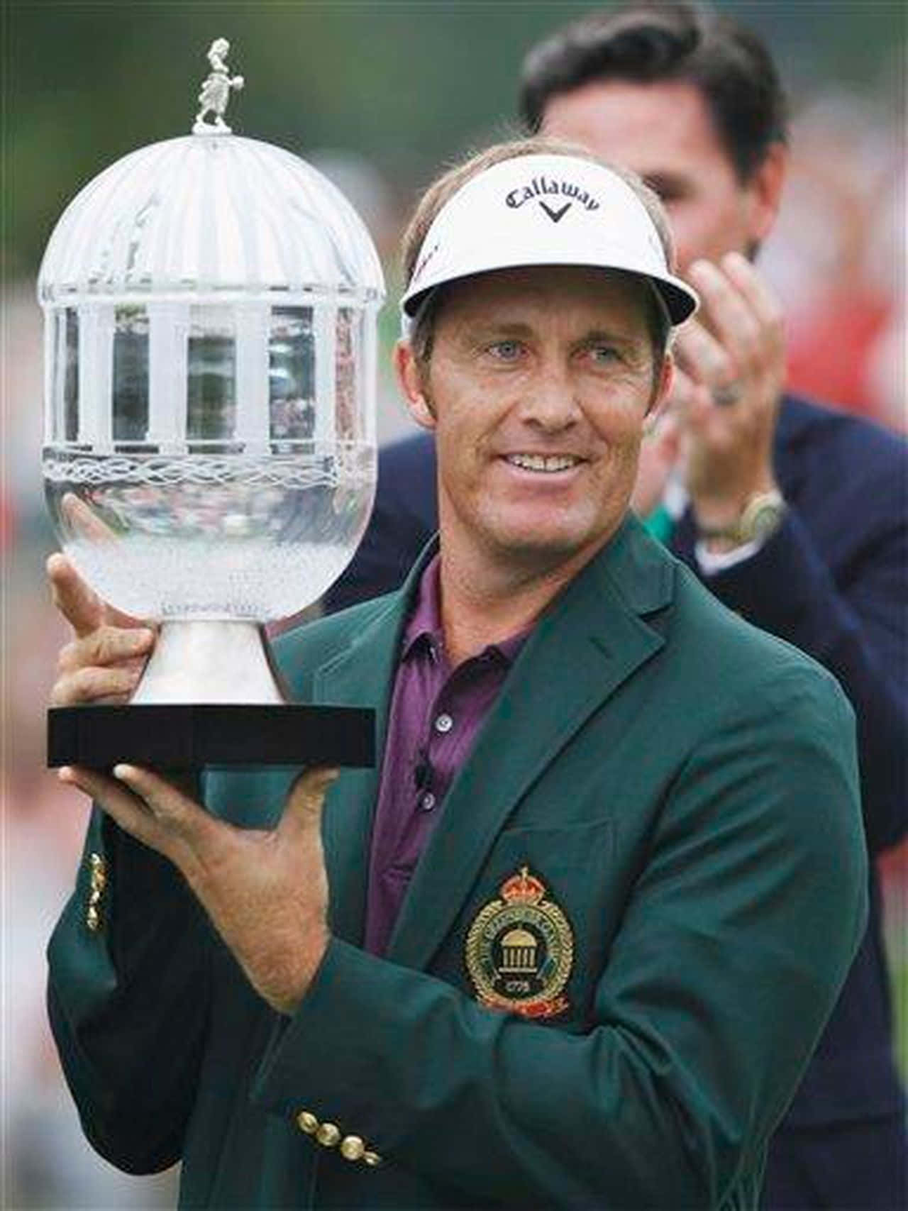 Trophy 桌布 壁紙 — 一位微笑的高爾夫球手穿著綠色外套，手持一個大型玻璃獎盃，頂部有一個高爾夫球手雕像。