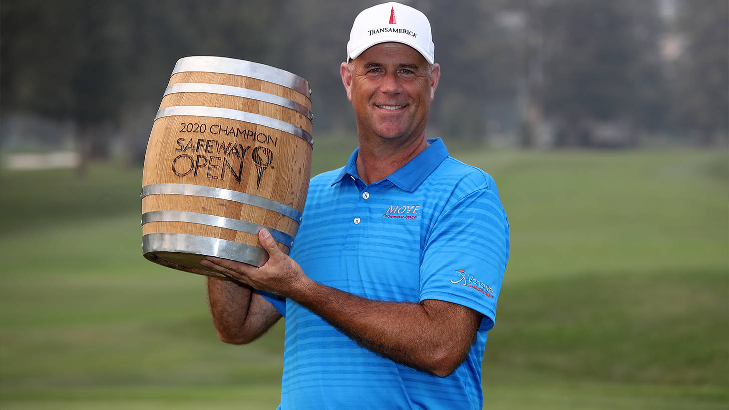 Champion 桌布 壁紙 — 一位微笑的高爾夫球手穿著藍色Polo衫，在綠色高爾夫球場上抱著一個刻有「2020 Champion Safeway Open」的木桶獎盃。