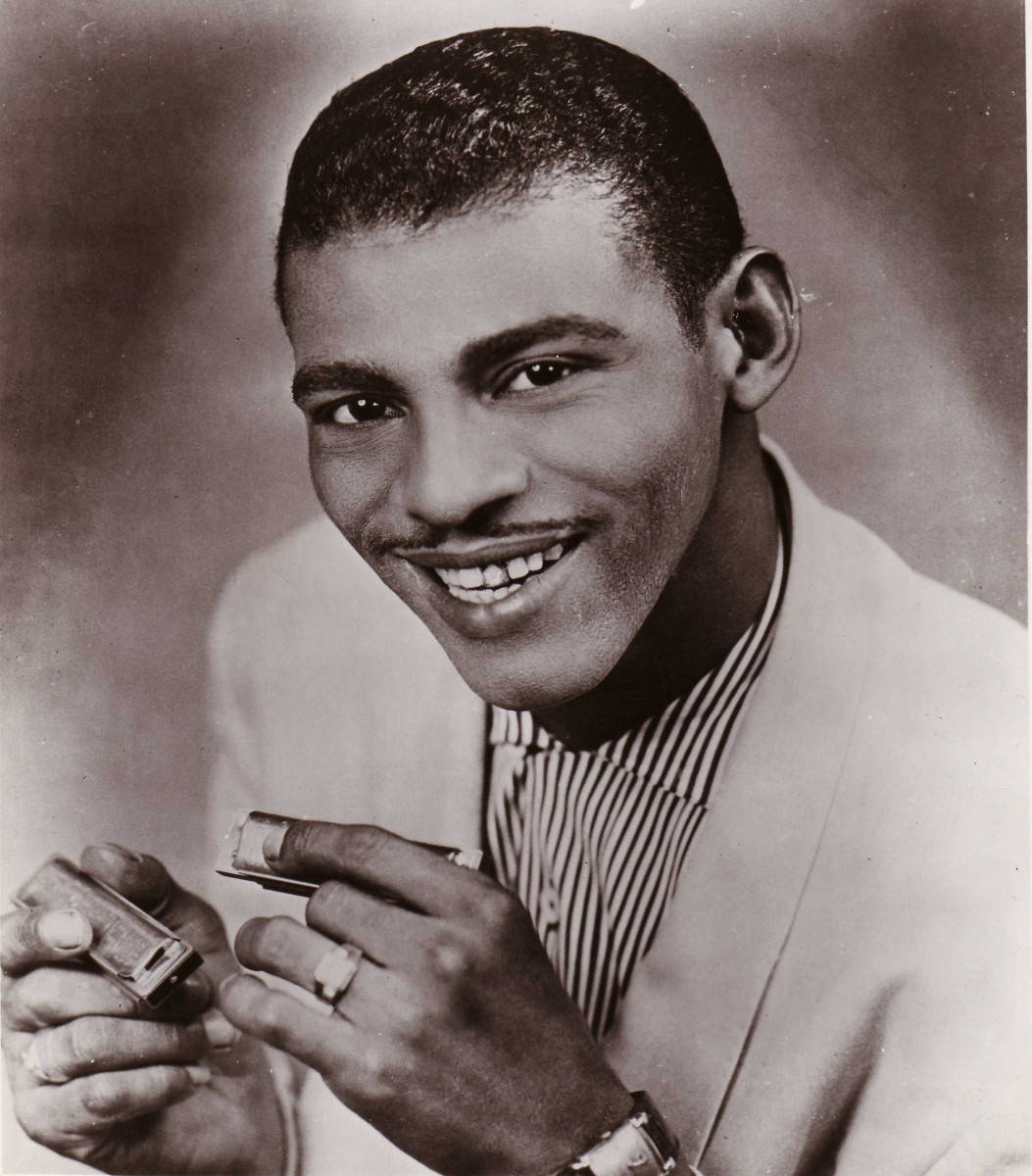 Little Walter 桌布 壁紙 — 一位微笑的黑人男士身穿淺色西裝和條紋襯衫，在復古工作室肖像中拿著口琴和打火機。