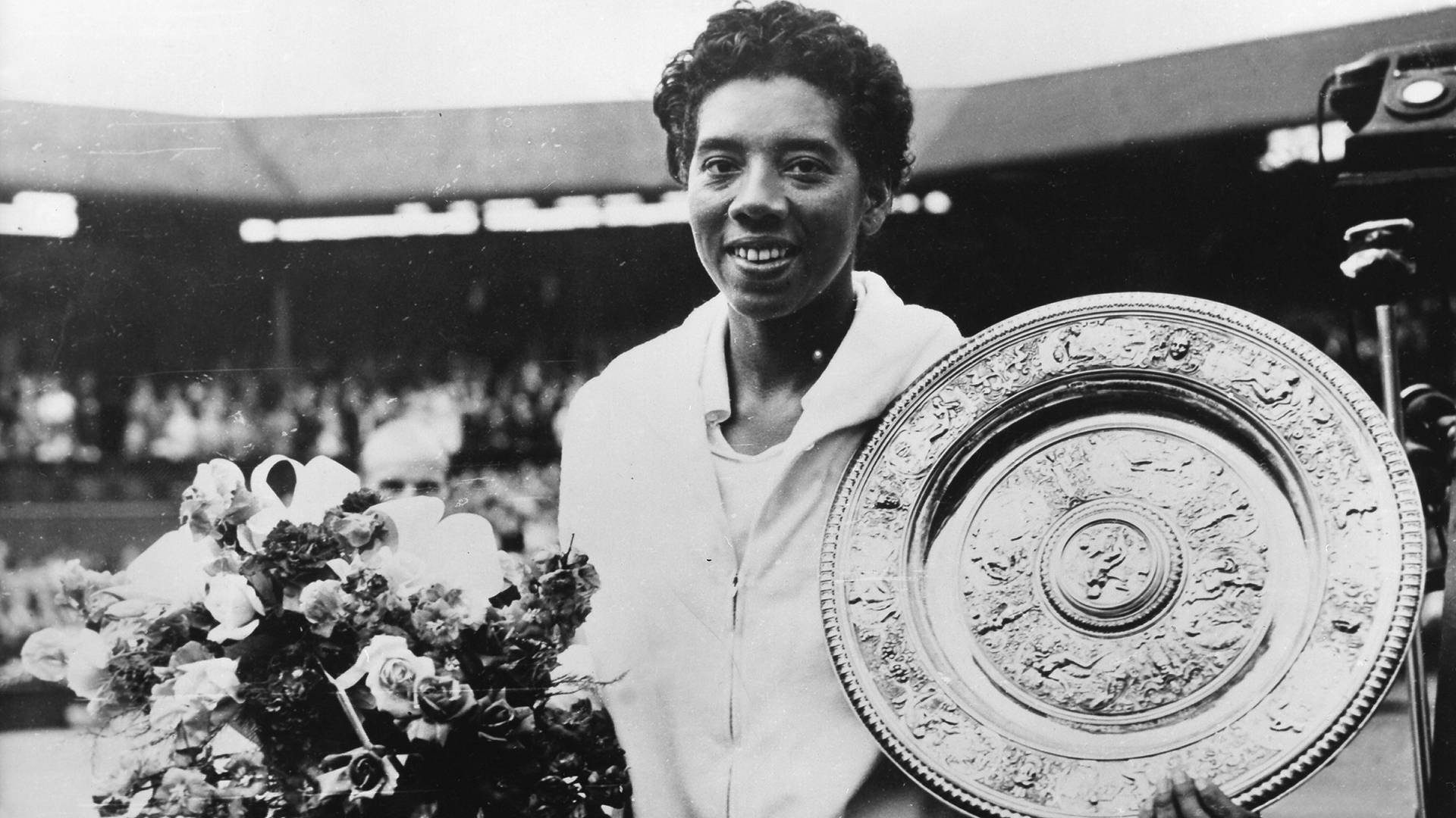 Tennis 桌布 壁紙 — 一位微笑的黑人網球冠軍在體育場球場上拿著一個大的華麗獎盃和一束鮮花。