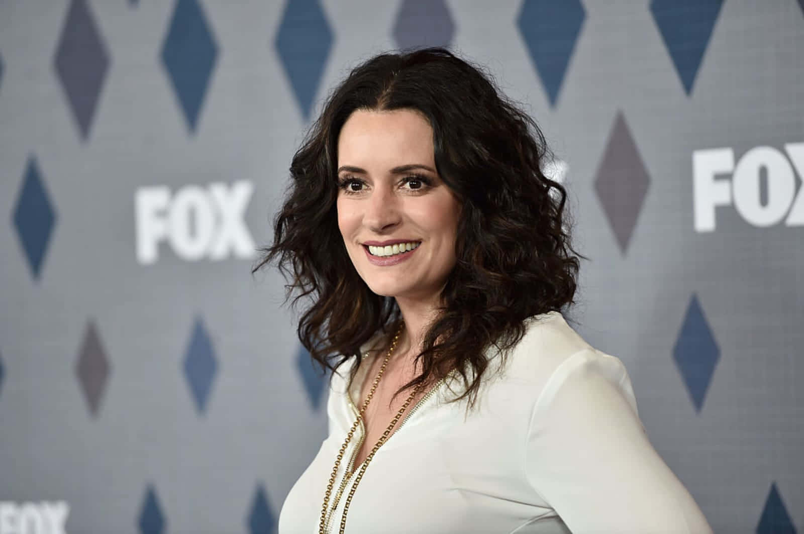 paget brewster 桌布 壁紙 — 一位微笑的黑捲髮女性穿著白色襯衫，在帶有鑽石圖案的FOX品牌背景前擺姿勢。