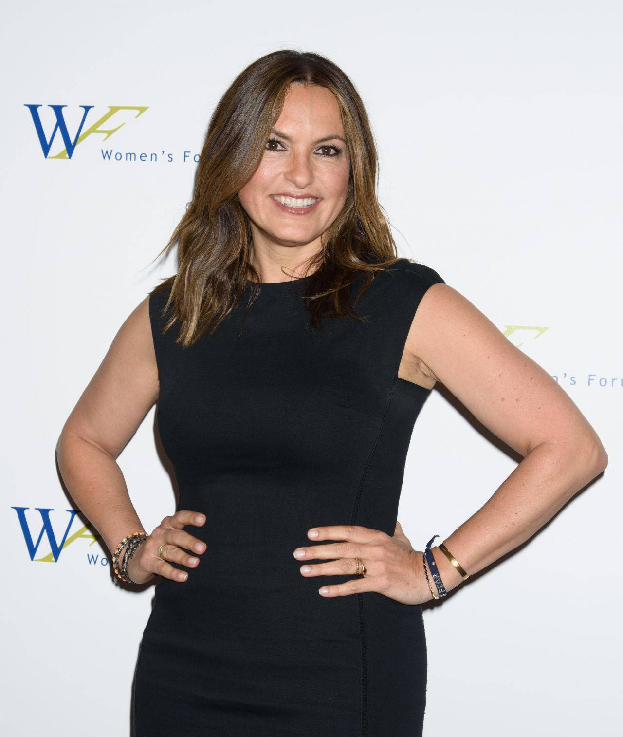 Celebrity 桌布 壁紙 — 一位微笑的黑裙女士自信地雙手叉腰，站在帶有Women's Forum標誌的白色背景前。