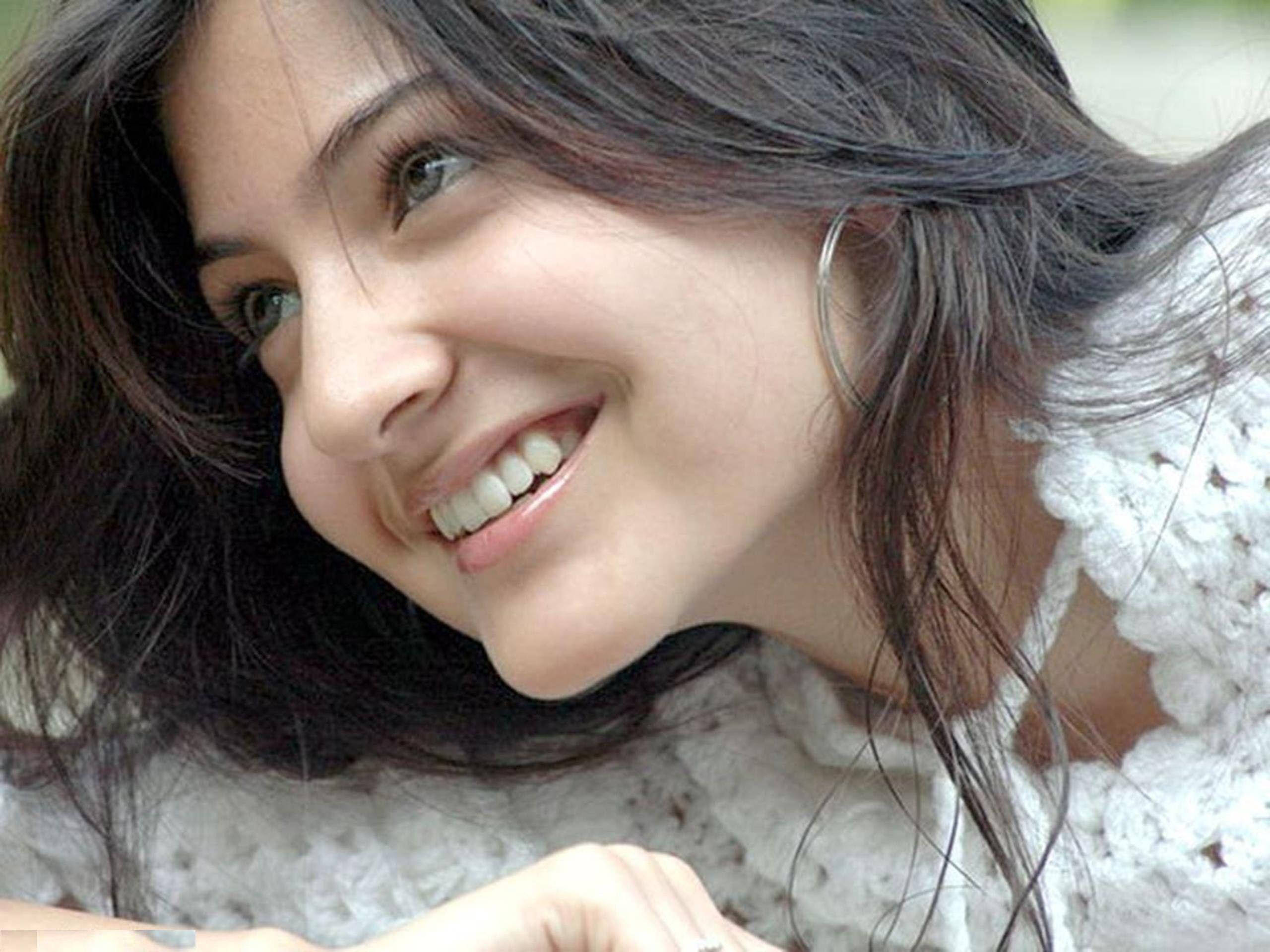 Anushka Sharma 桌布 壁紙 — 一位微笑的黑髮亮眼女性穿著白色針織上衣的特寫。