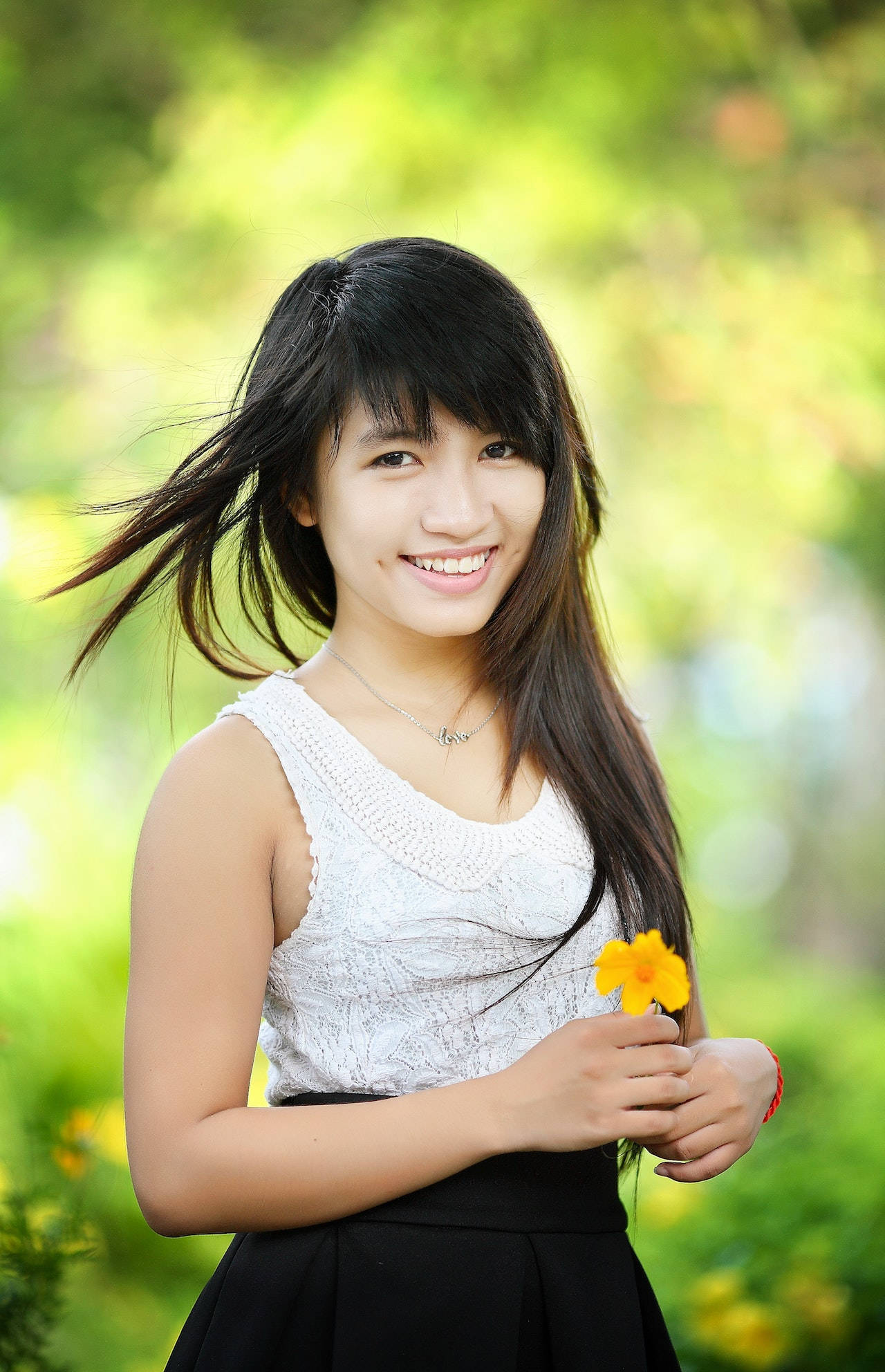 smiling 桌布 壁紙 — 一位微笑的黑髮年輕女性在明亮的綠色模糊花園背景下手持一朵黃色花朵。