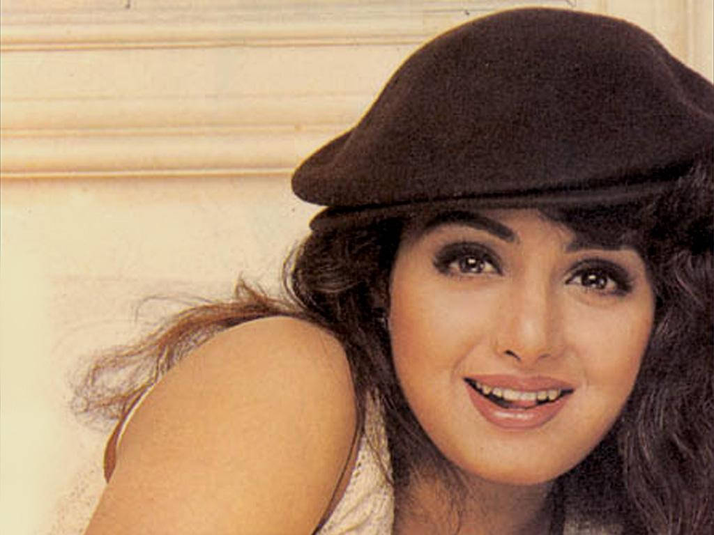 Sridevi 桌布 壁紙 — 一位微笑的黑髮曲髮女性戴著黑色貝雷帽，背景是帶有線條的米色牆壁。