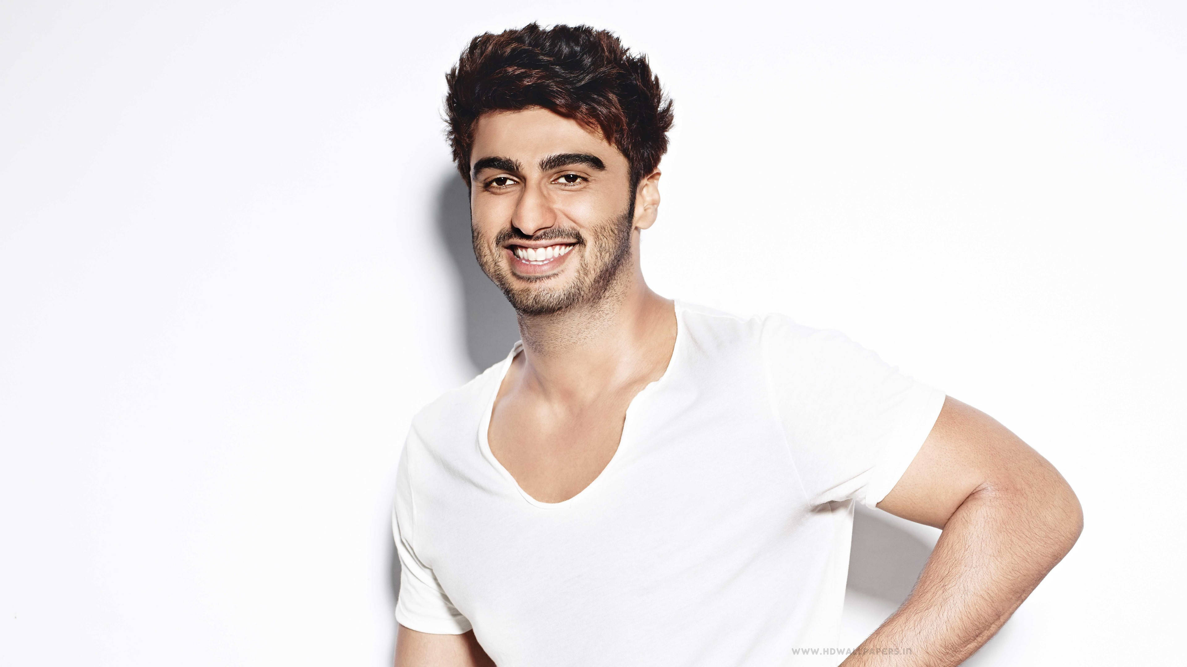 Arjun Kapoor 桌布 壁紙 — 一位微笑的黑髮鬍鬚男士穿著白色T恤，背景是純白色。