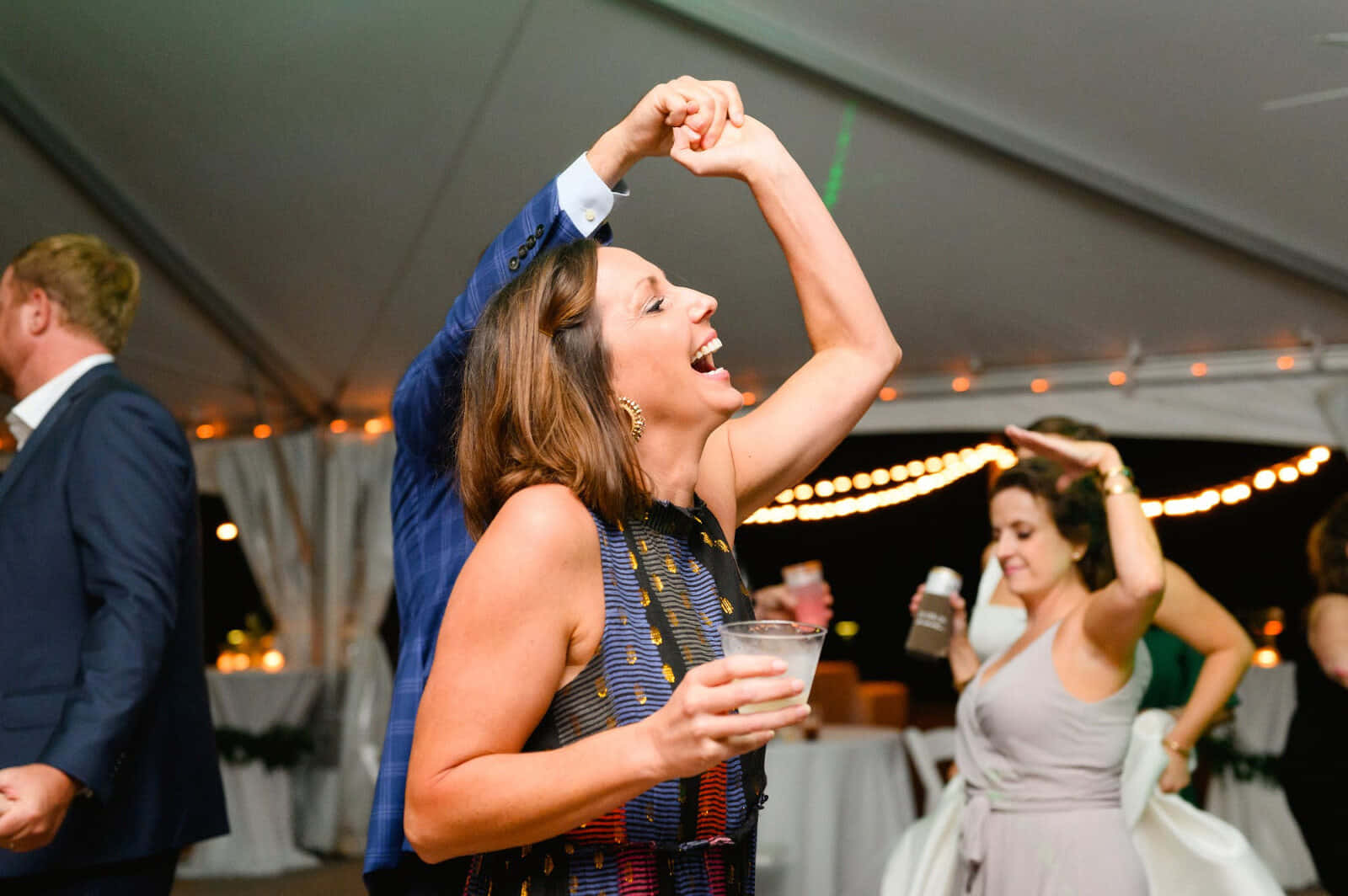 party dance 桌布 壁紙 — 一位快樂的女人在夜間的節日帳篷裡，在燈串下舉起手臂笑著跳舞。