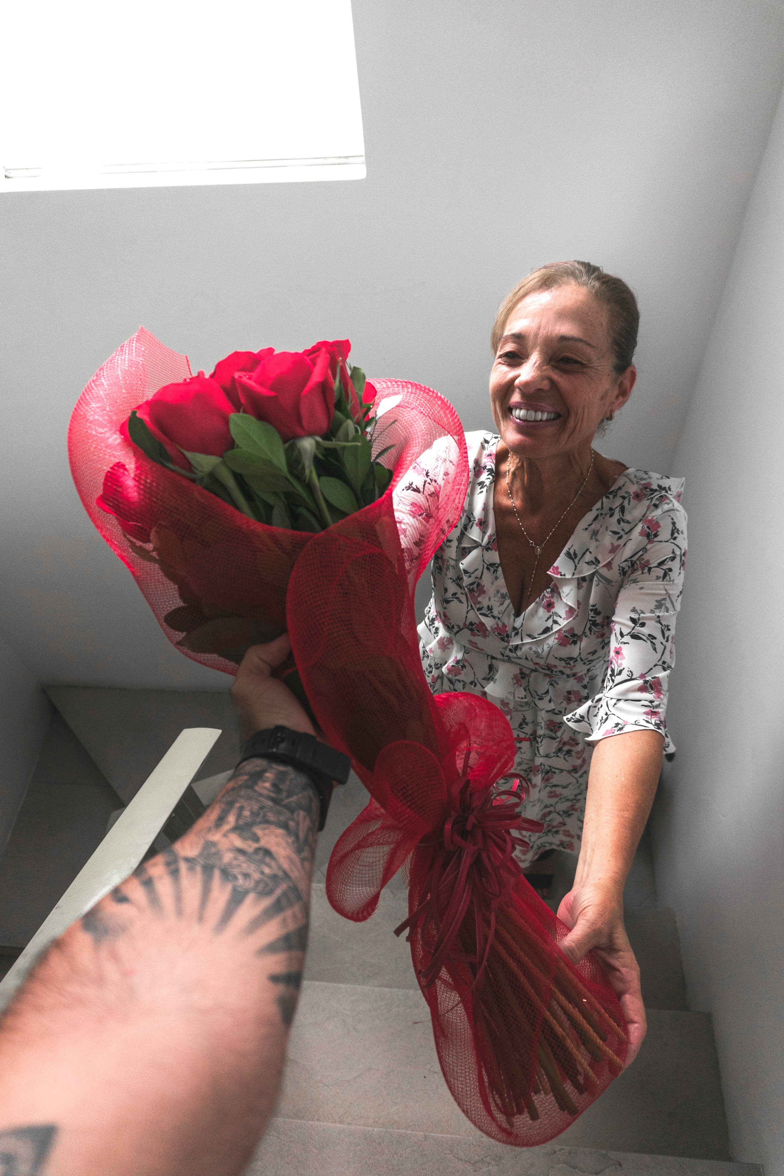 Mothers Day 桌布 壁紙 — 一位快樂的女人在樓梯上溫暖地微笑，同時收到一束用紅色網包裹的鮮豔紅玫瑰花束。