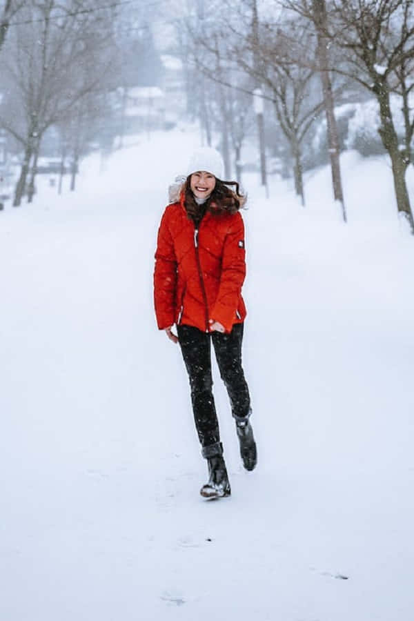 Snowshoes 桌布 壁紙 — 一位快樂的女人穿著鮮紅色冬季外套和白色毛帽，在一個有裸樹和飄落雪花的雪地公園裡跳躍。