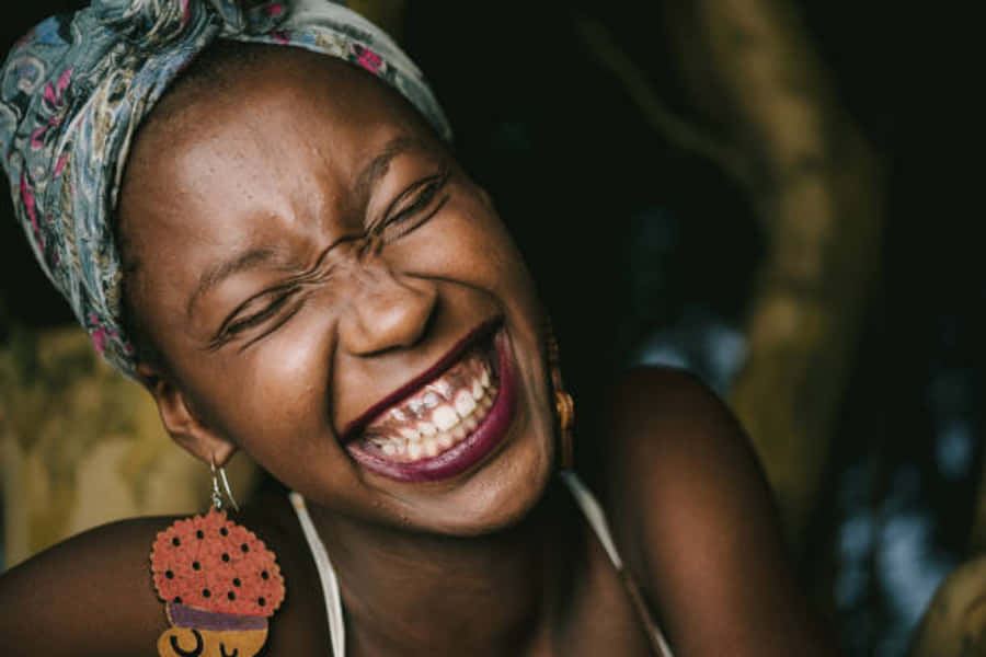 Nigeria 桌布 壁紙 — 一位快樂的女人閉著眼睛開懷大笑，戴著圖案頭巾和彩色耳環。