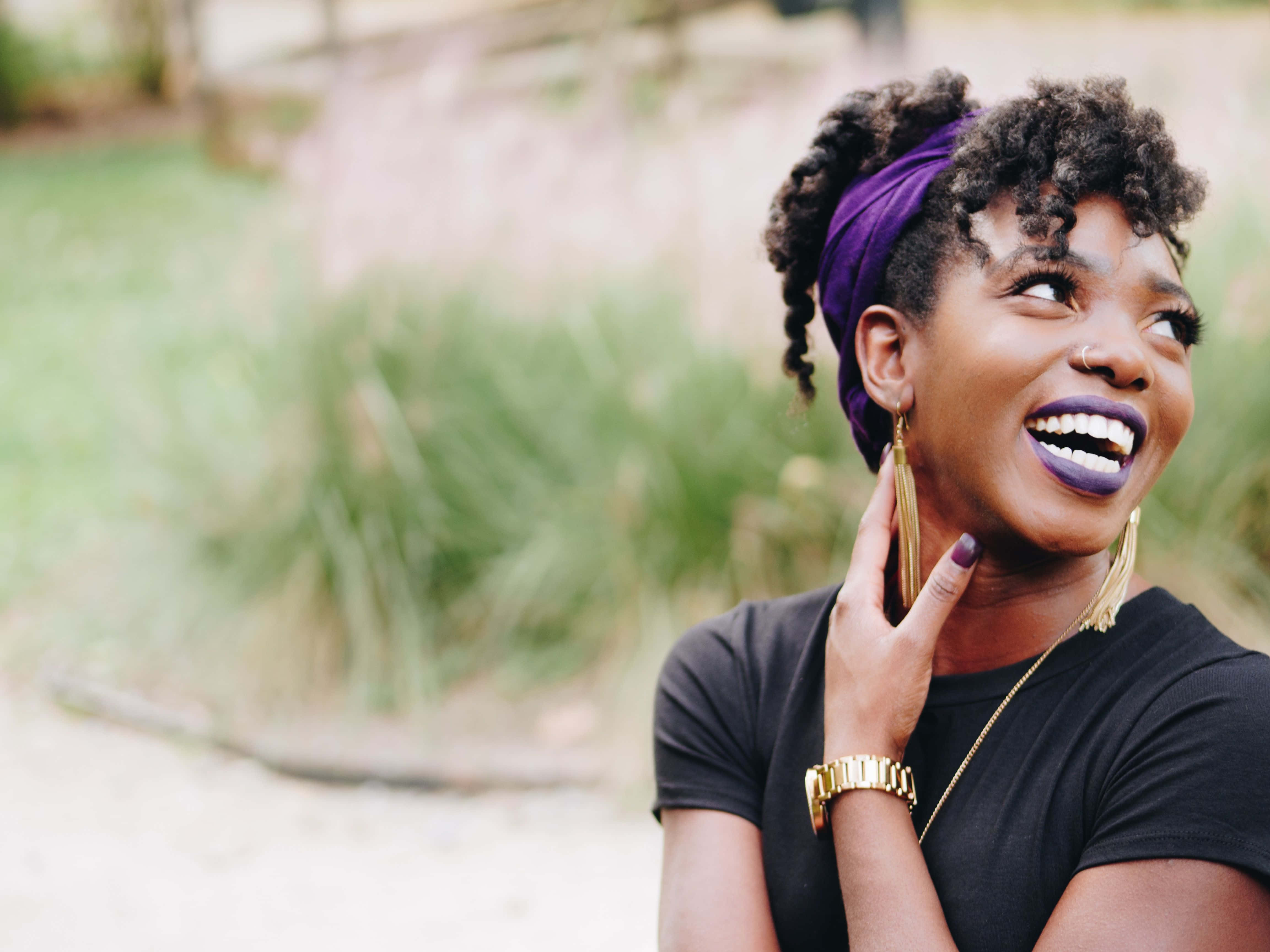 Black Girl Magic 桌布 壁紙 — 一位快樂的女士，捲髮，戴著紫色頭巾，在自然光下開懷大笑。