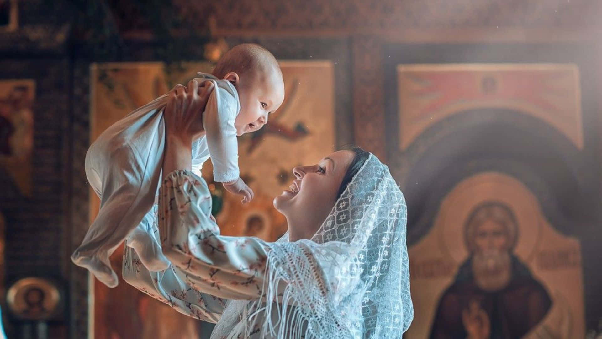 Baby 桌布 壁紙 — 一位快樂的女士在教堂裡高舉她的嬰兒，對著金色的宗教圖標溫暖地微笑。