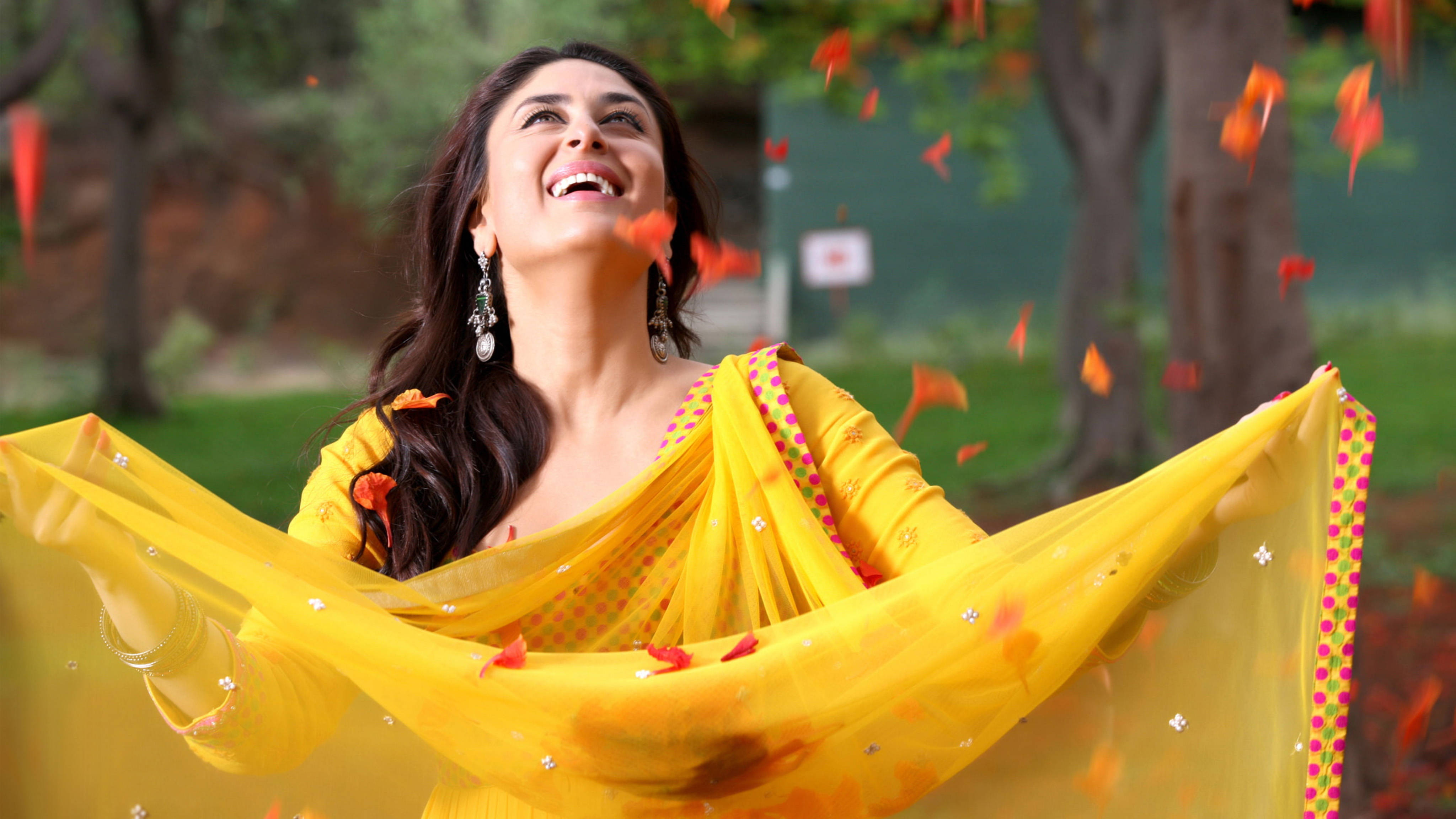 Kareena 桌布 壁紙 — 一位快樂的女子穿著鮮黃色紗麗，在陽光明媚的公園裡，秋葉旋轉環繞，她開懷大笑。