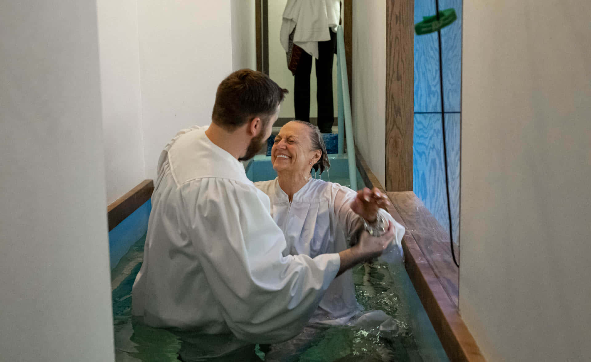 Baptism 桌布 壁紙 — 一位快樂的女性在教堂的木製洗禮盆中由神職人員施洗時微笑。