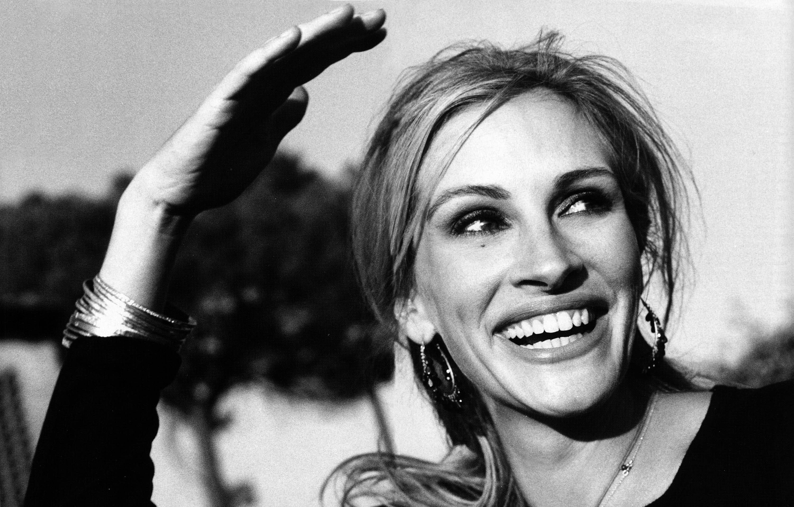 Julia Roberts 桌布 壁紙 — 一位快樂的女性在黑白肖像中，舉起手遮擋陽光，笑得燦爛。
