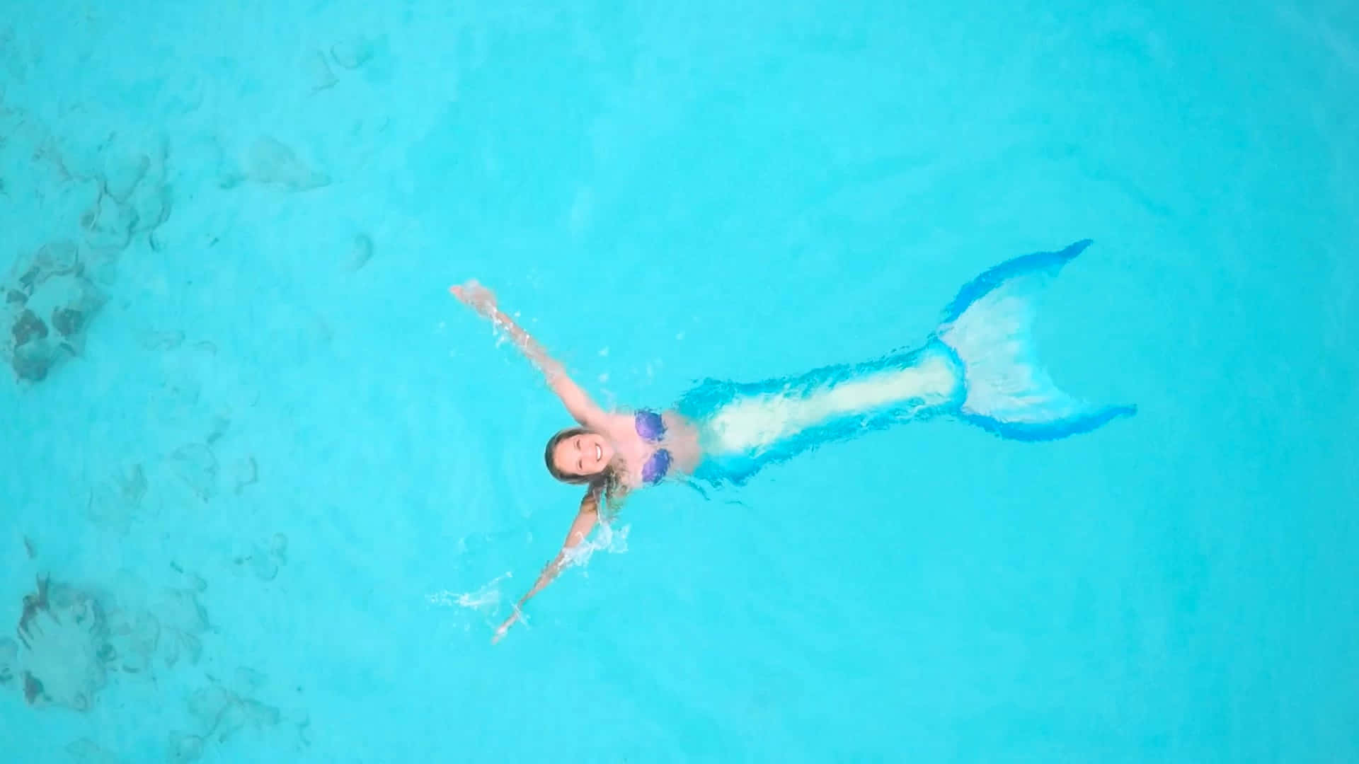Real Mermaid 桌布 壁紙 — 一位快樂的女性穿著藍色美人魚尾巴，在清澈的碧綠水中仰面漂浮。