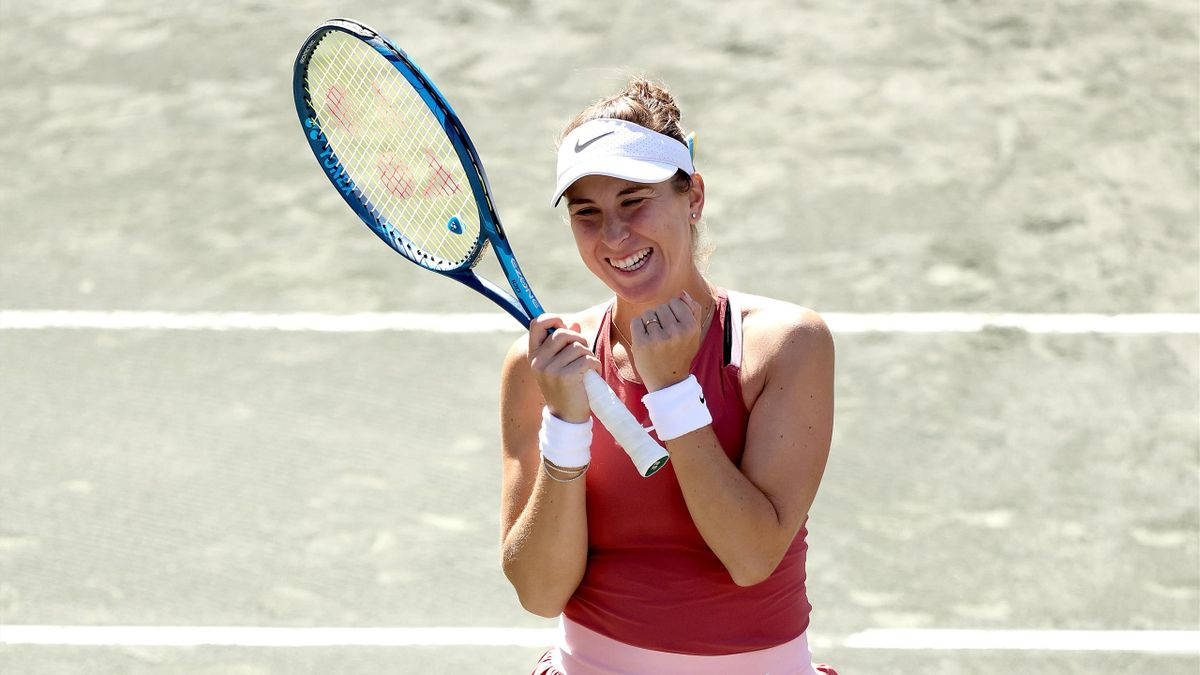 Excited 桌布 壁紙 — 一位快樂的女網球選手在陽光普照的硬地球場上，帶著勝利的笑容高舉球拍慶祝勝利。