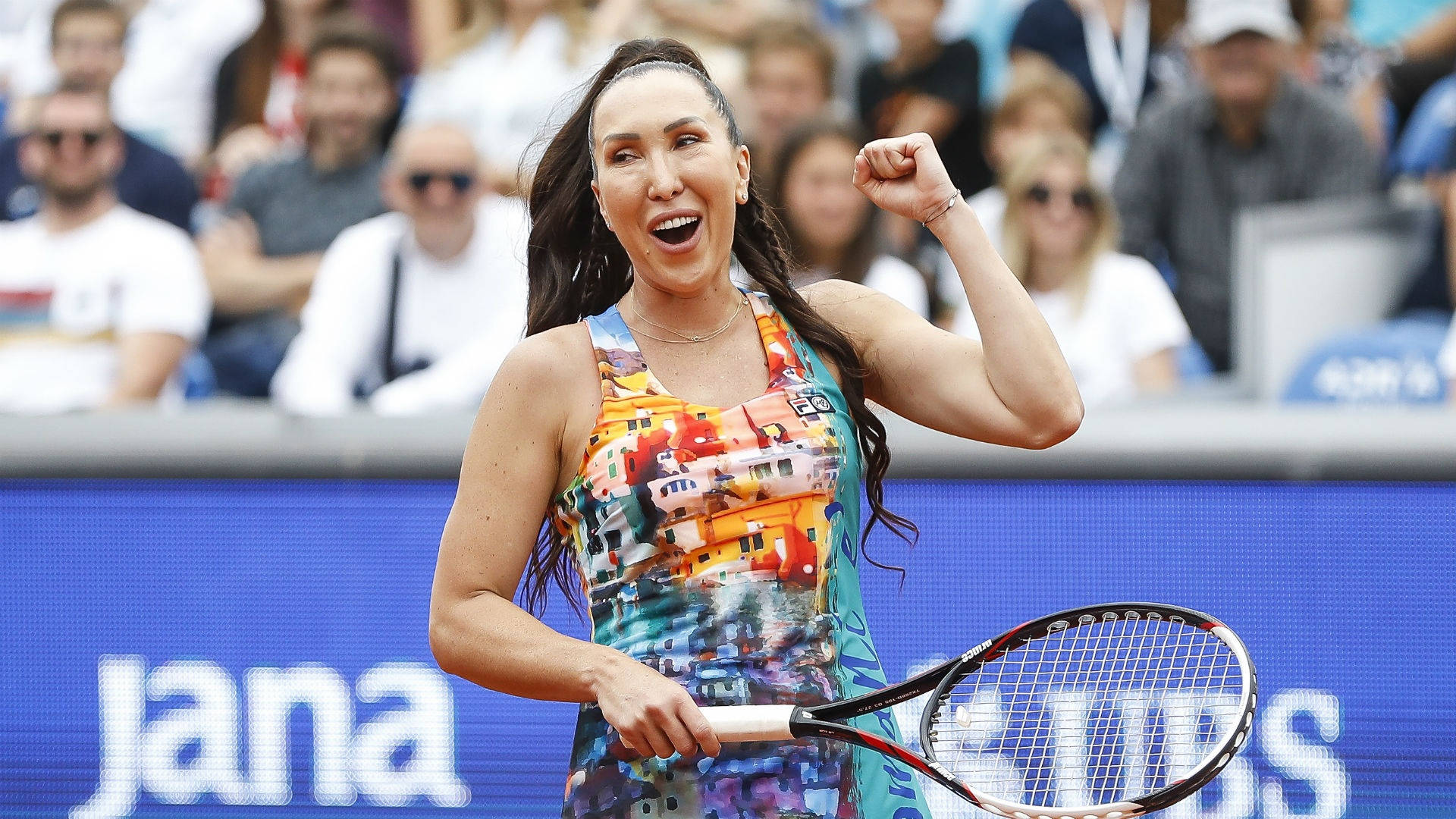 Tennis 桌布 壁紙 — 一位快樂的女網球選手在陽光普照的球場上高舉拳頭慶祝勝利，觀眾在她身後歡呼。