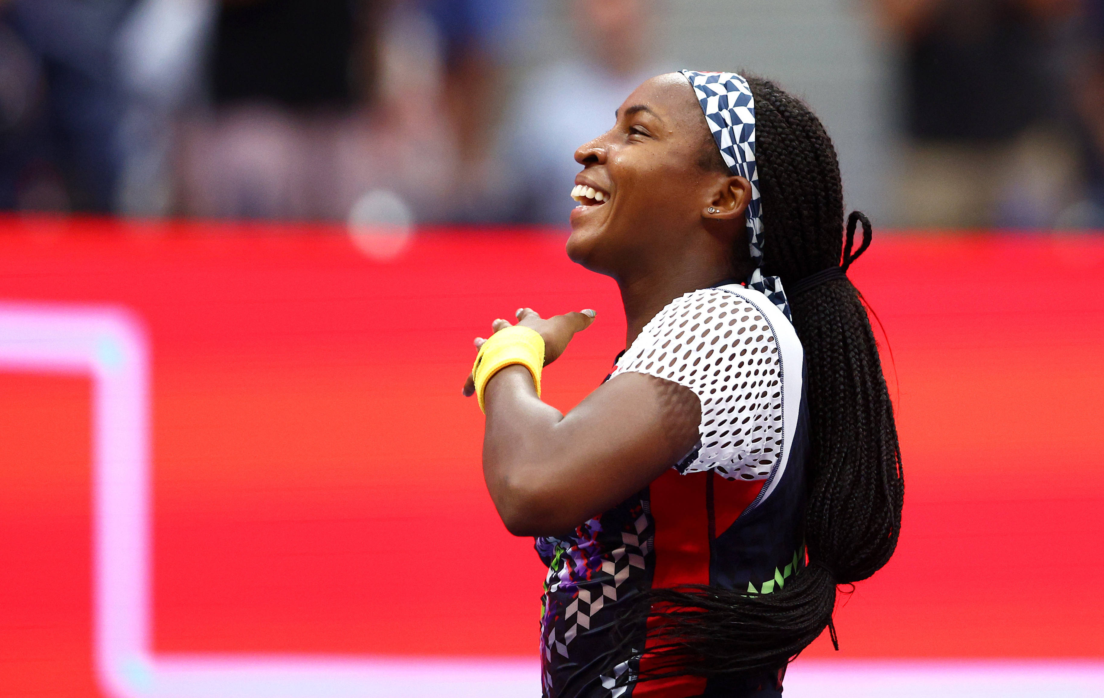 Coco Gauff 桌布 壁紙 — 一位快樂的女網球選手在鮮紅的球場背景下，雙手交握在胸前，露出燦爛的笑容。