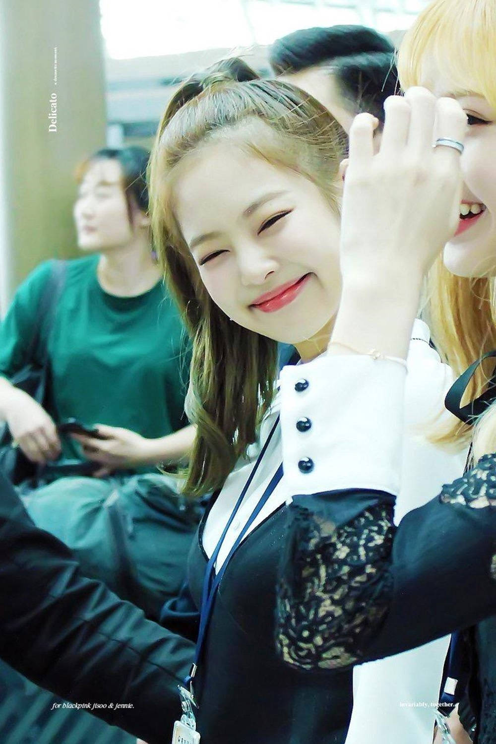 BLACKPINK 桌布 壁紙 — 一位快樂的年輕女子，波浪般的頭髮，在繁忙的室內環境中燦爛微笑並揮手。