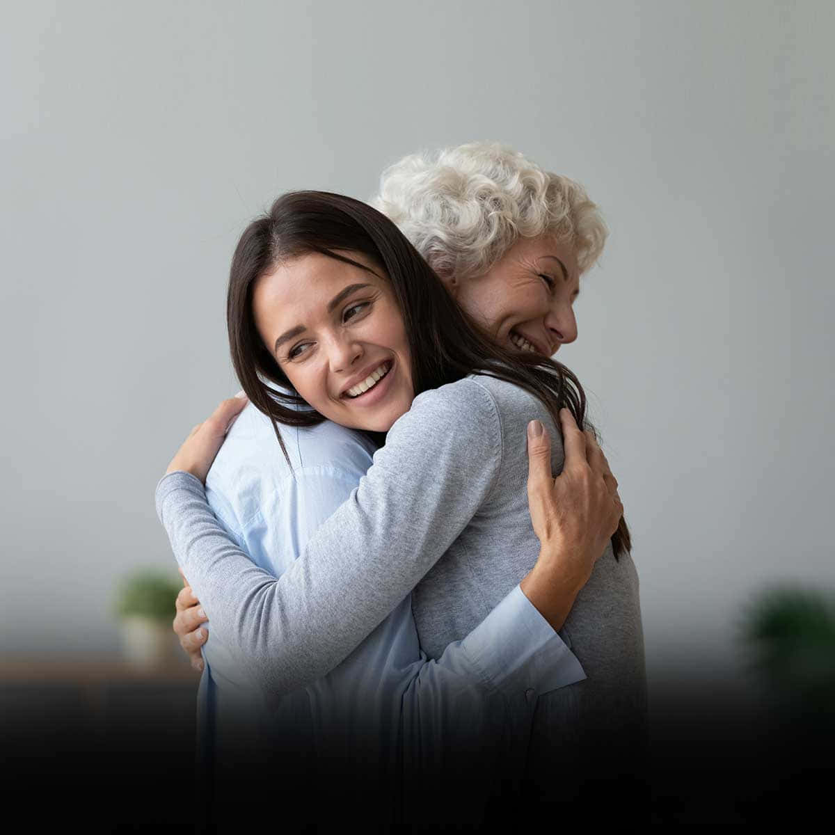 Hug 桌布 壁紙 — 一位快樂的年輕女子在柔和的灰色背景下，用溫暖真摯的擁抱擁抱她微笑的年邁母親。