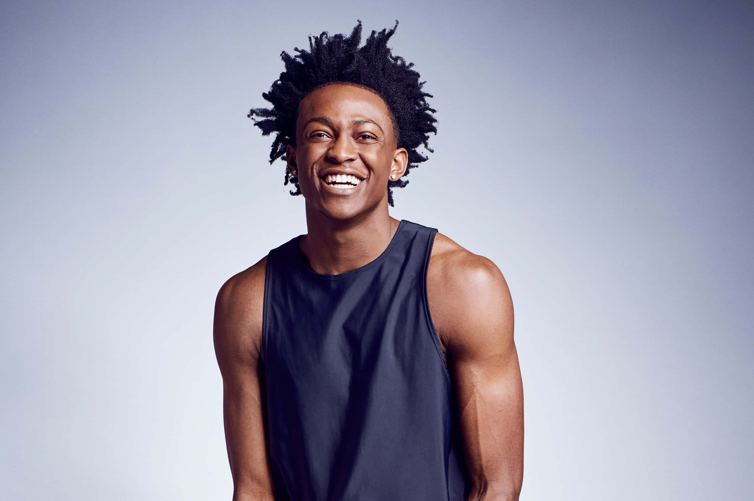 NBA 桌布 壁紙 — 一位快樂的年輕男子留著非洲式頭髮，穿著深色背心，在柔和的漸變工作室背景前閃耀。