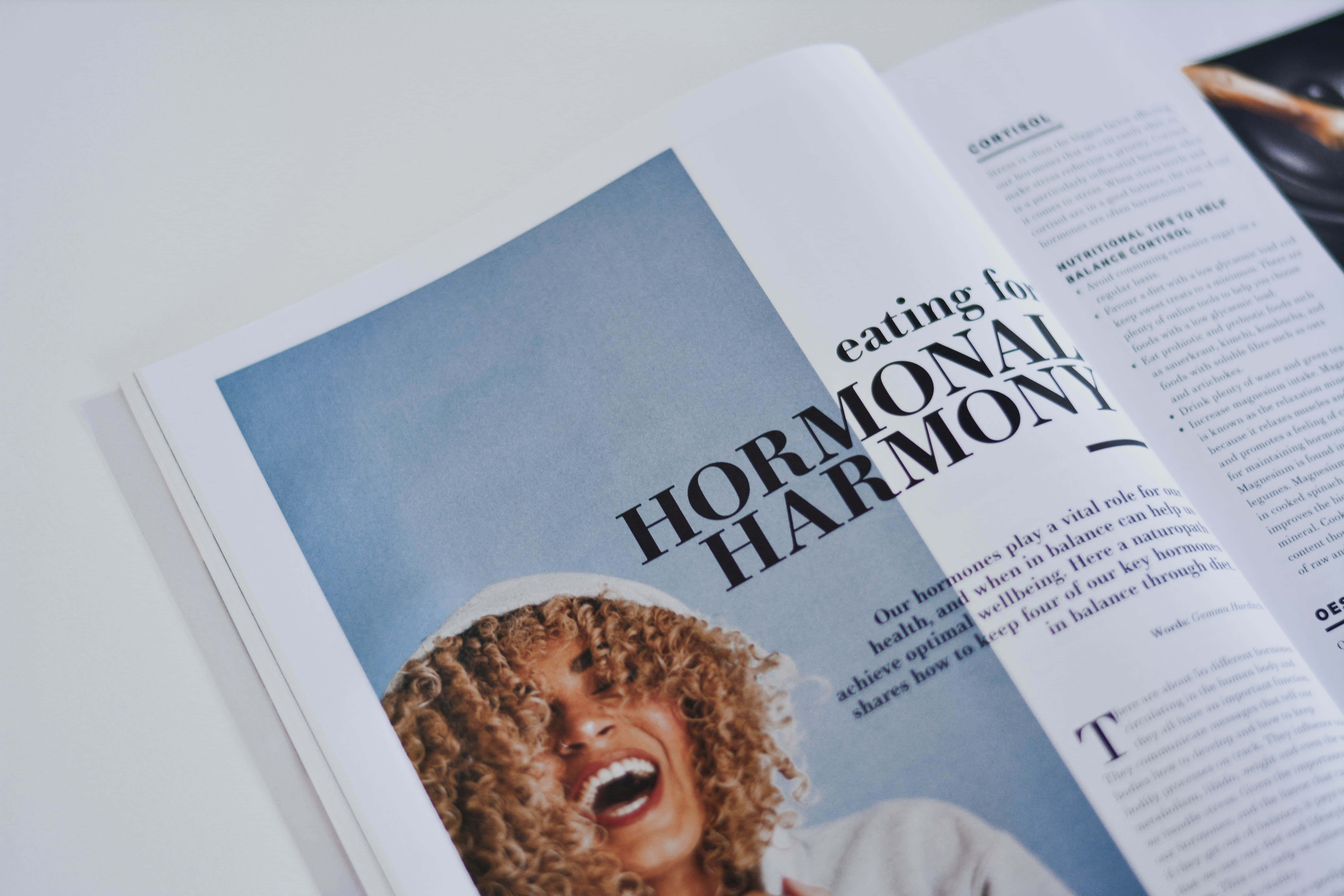 雜誌 桌布 壁紙 — 一位快樂的捲髮女性在名為「Hormonal Harmony」的雜誌跨頁上，對著柔和的藍色背景開懷大笑。